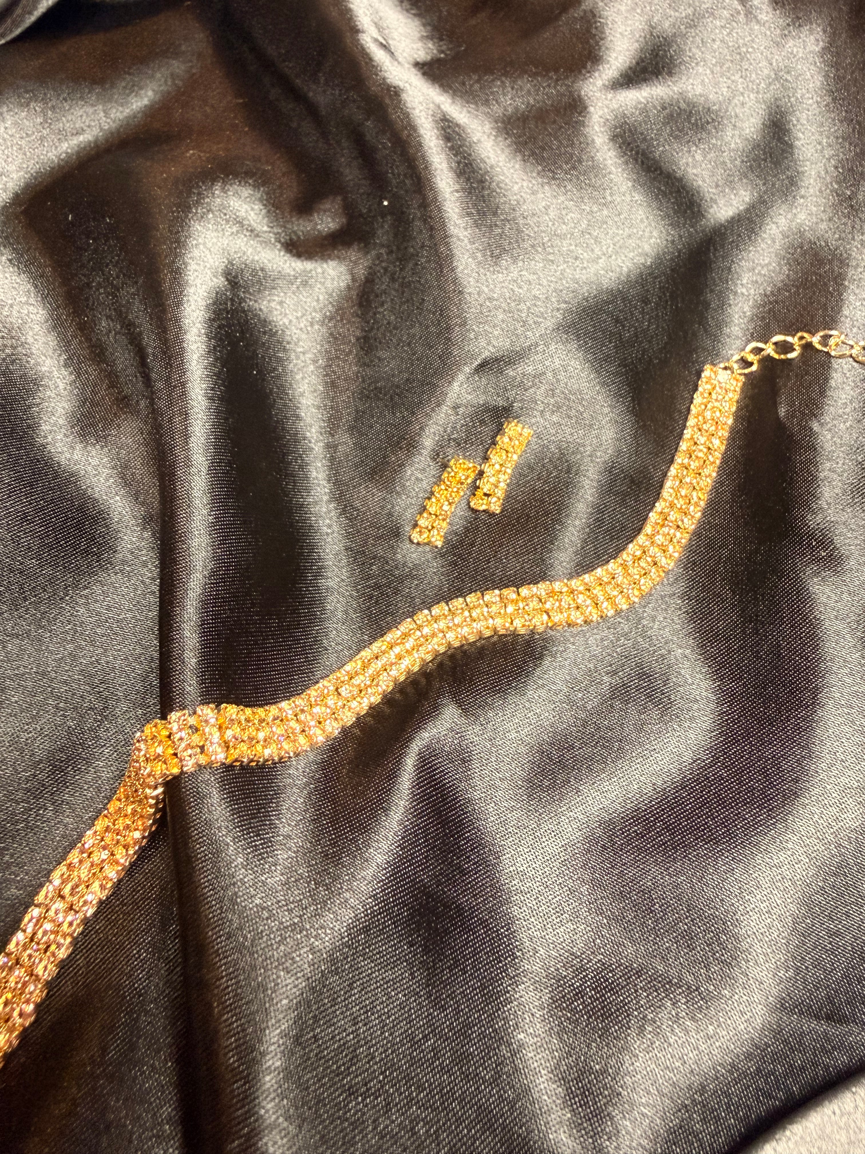 Gold necklace and earrings on a dark satin surface