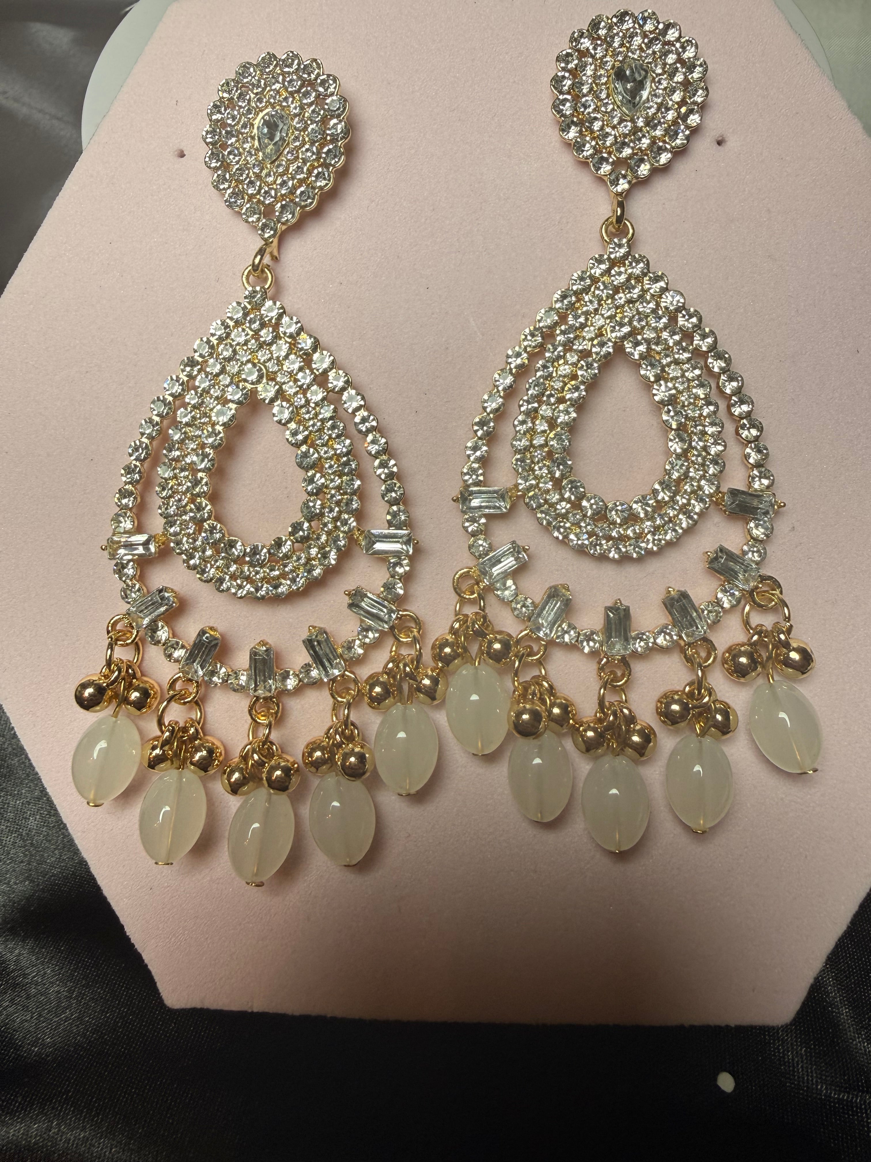 Pair of ornate earrings with gemstones on a pink surface