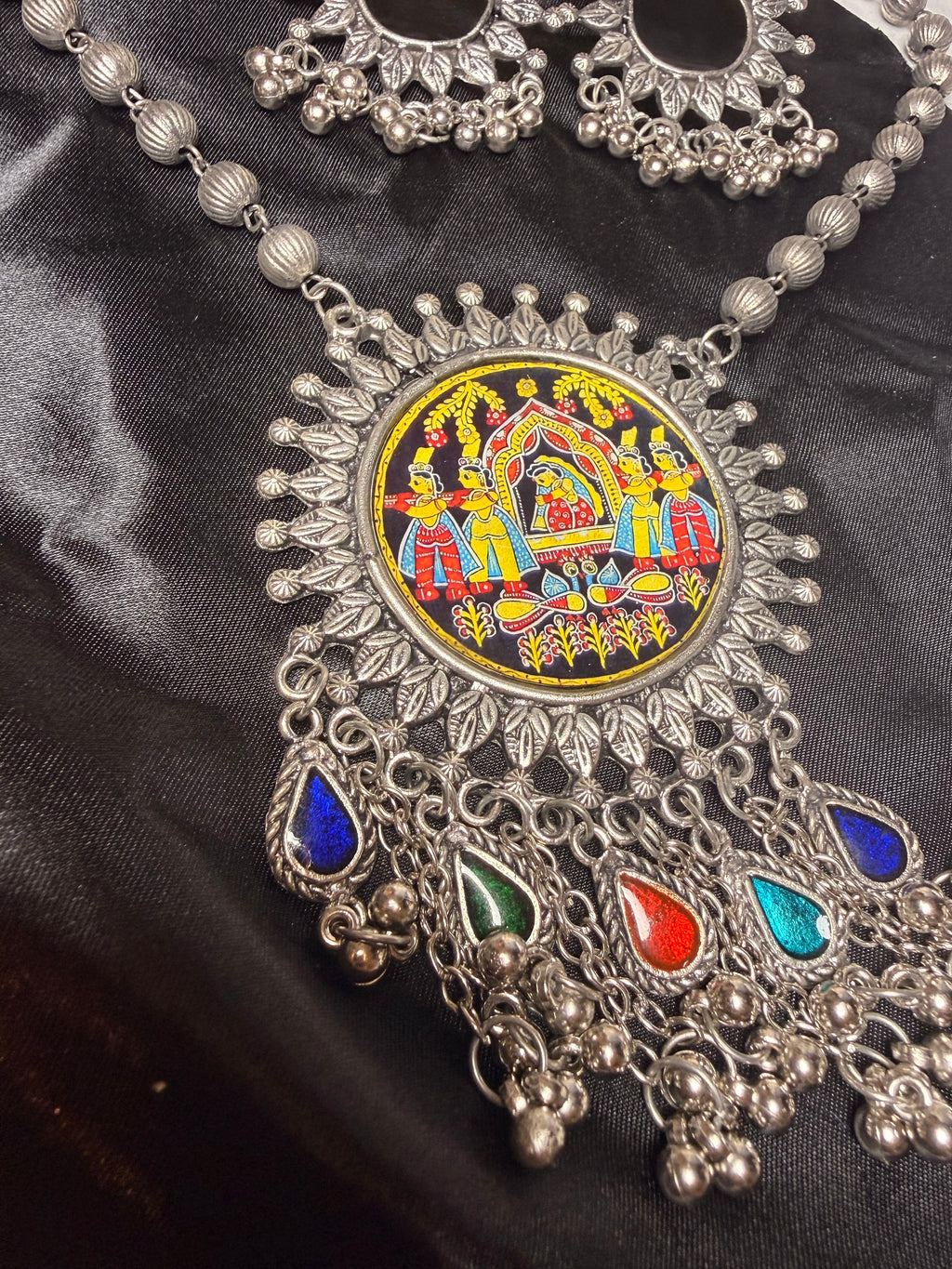 Decorative silver necklace with colorful gemstones on a black fabric background