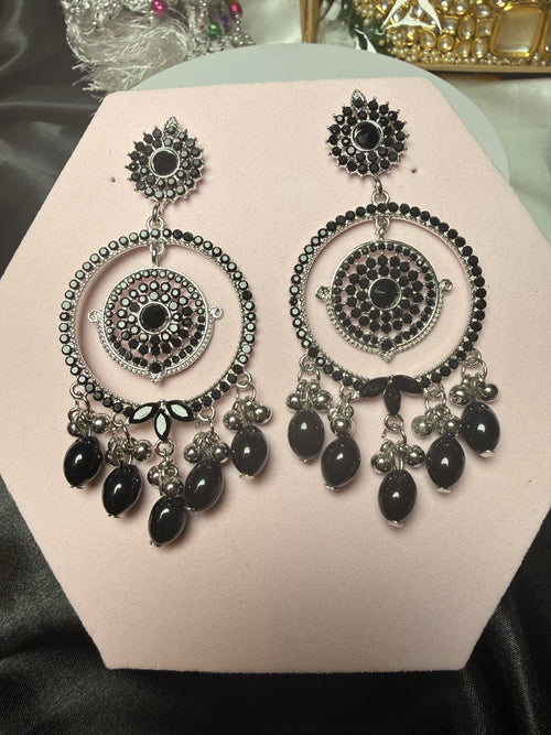 Pair of silver and black earrings on a pink stand