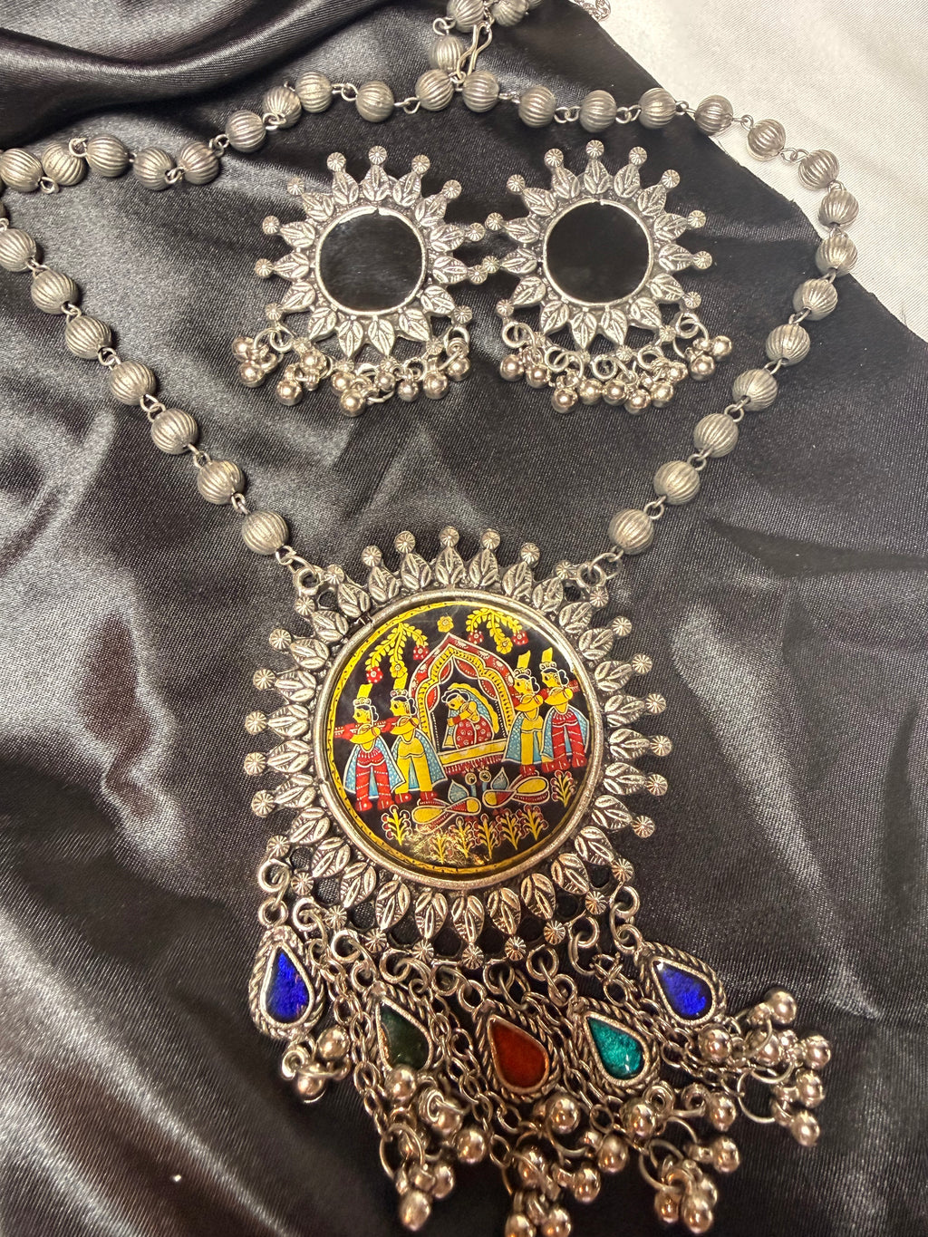 Ornate necklace with colorful central design on a dark fabric background