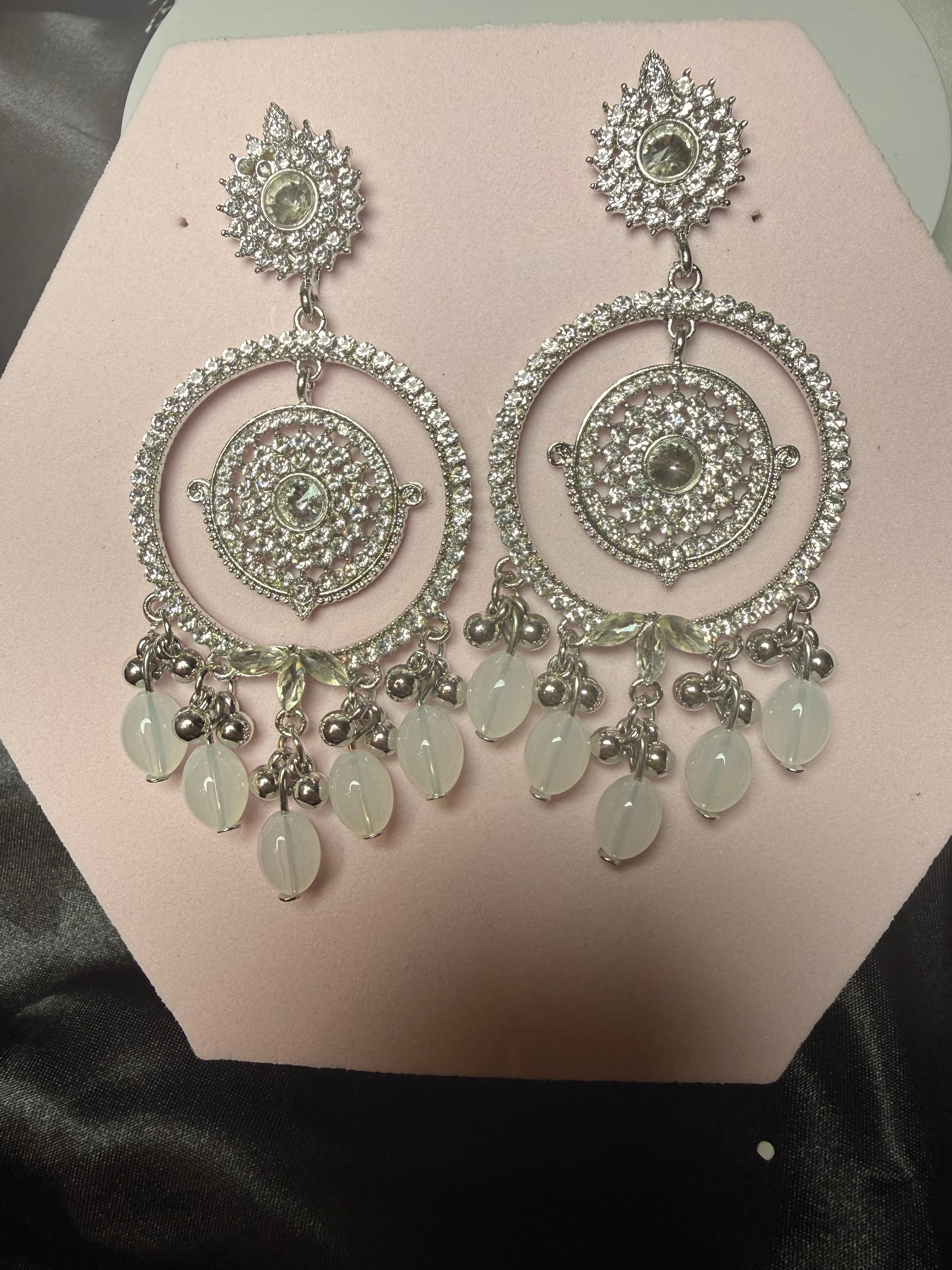 Pair of silver earrings with green beads on a pink stand.