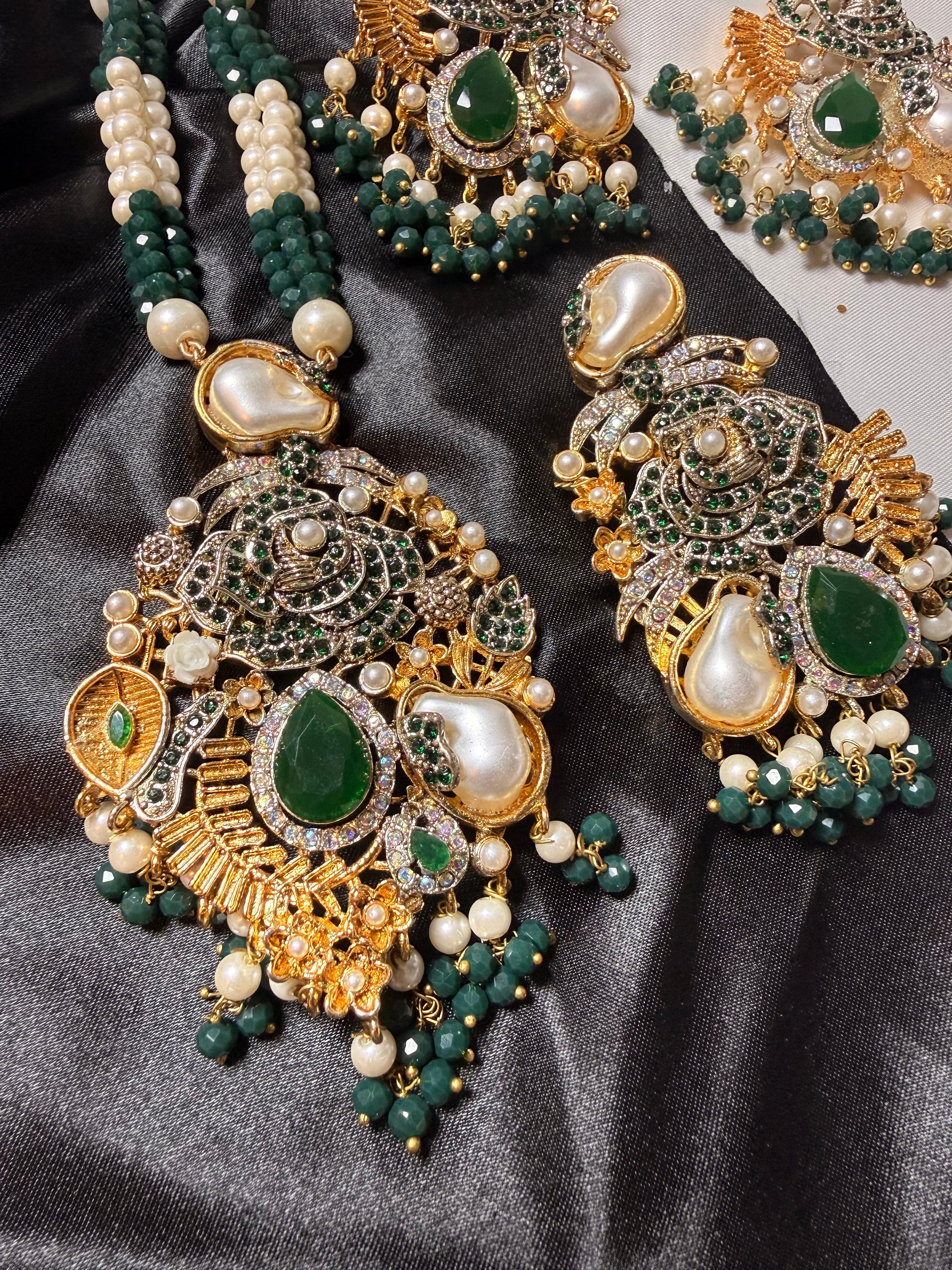 Ornate gold, green, and pearl jewelry set on a dark fabric background