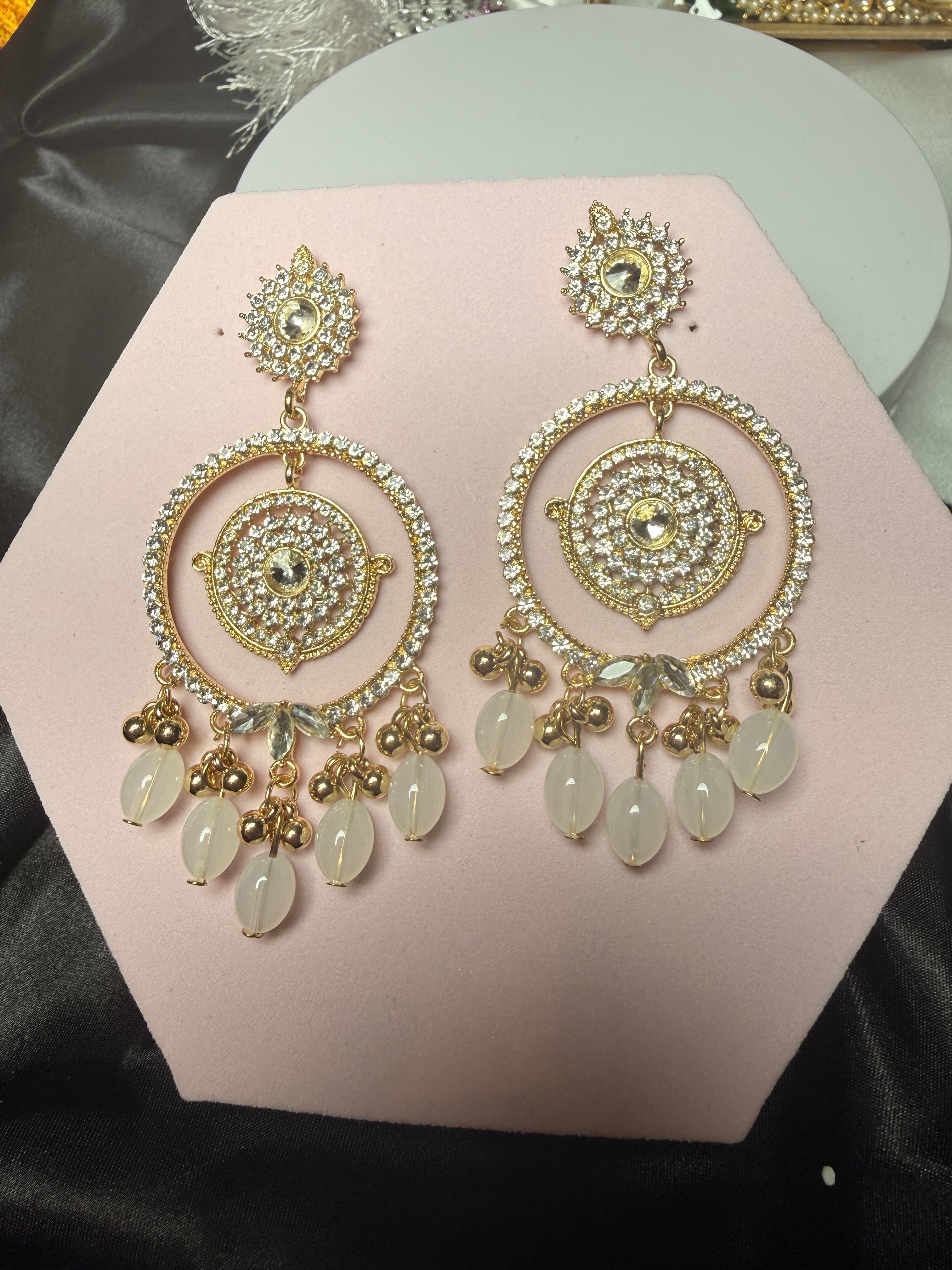 Gold and crystal earrings on a pink stand with a black background