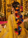 Woman in a yellow traditional outfit with colorful decorative hairpiece against a festive background.