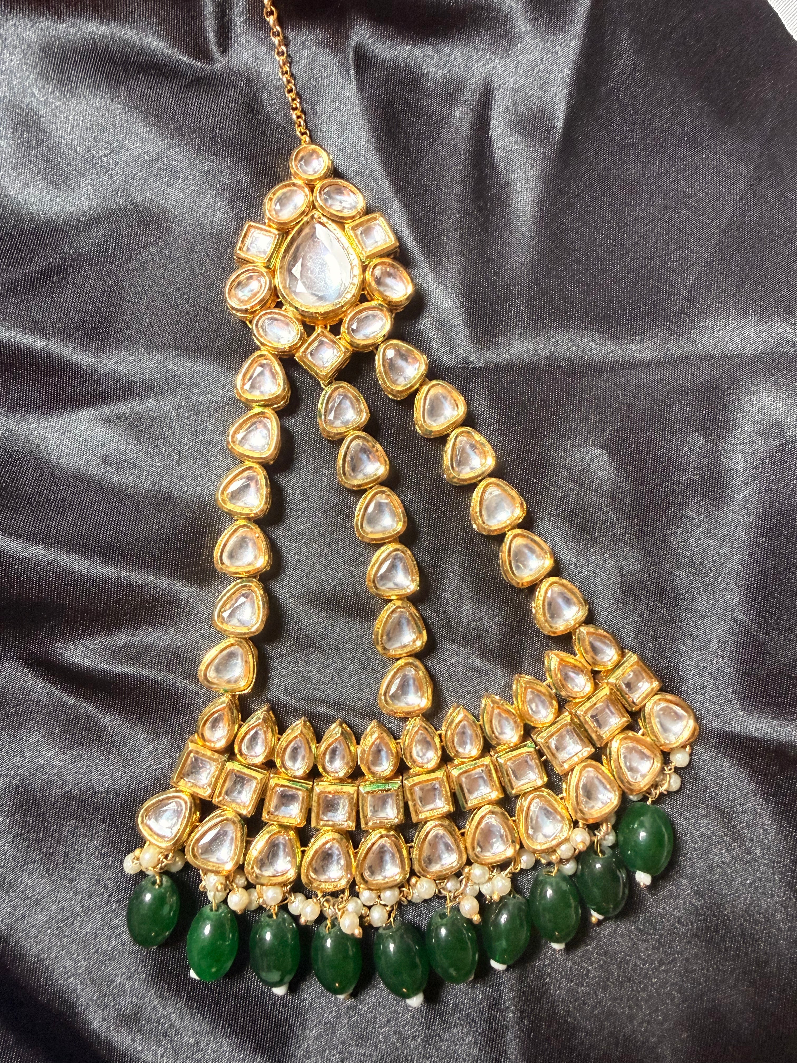 Ornate gold and green necklace on a gray fabric background