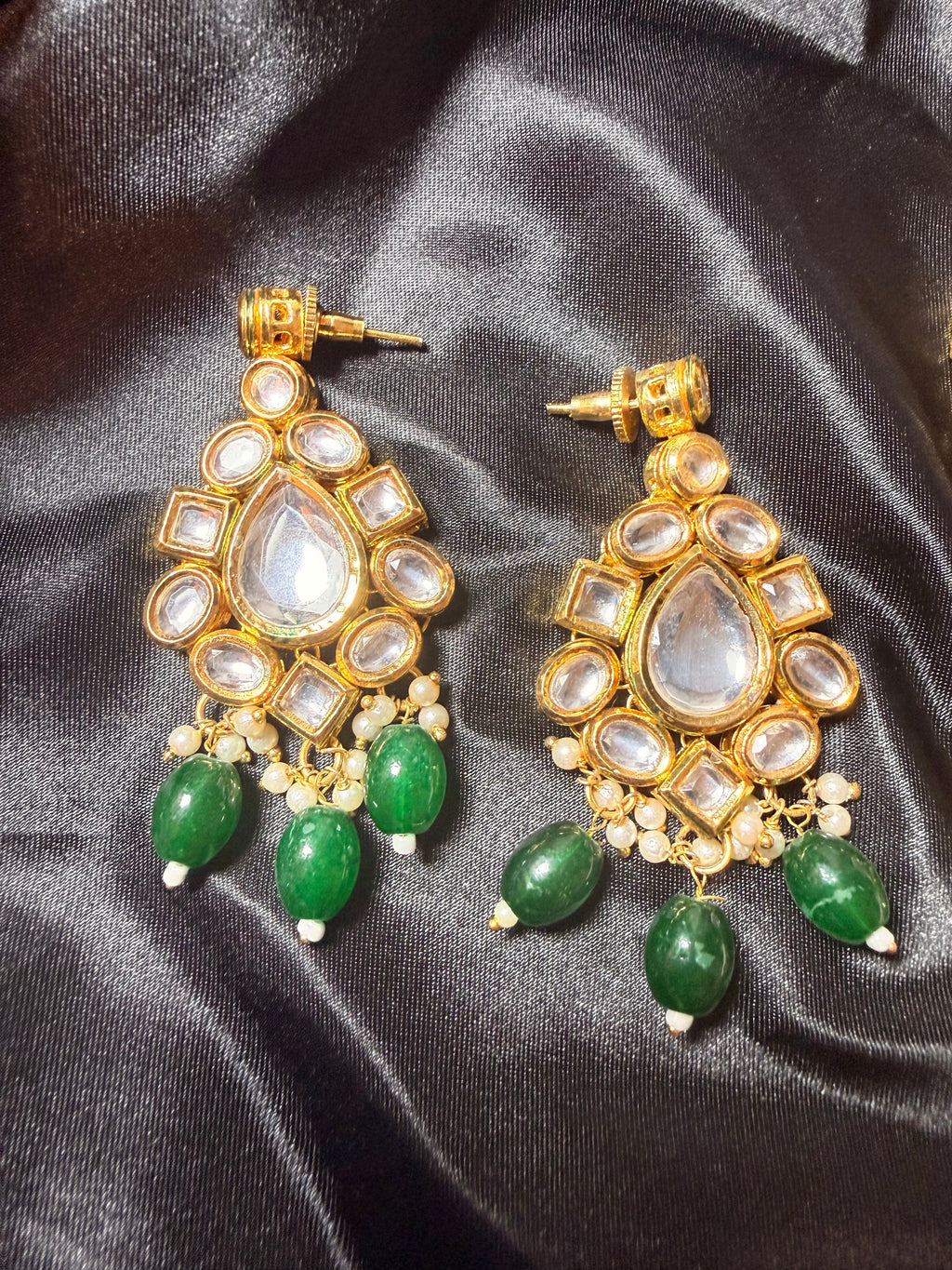 Gold and green earrings on a black satin background