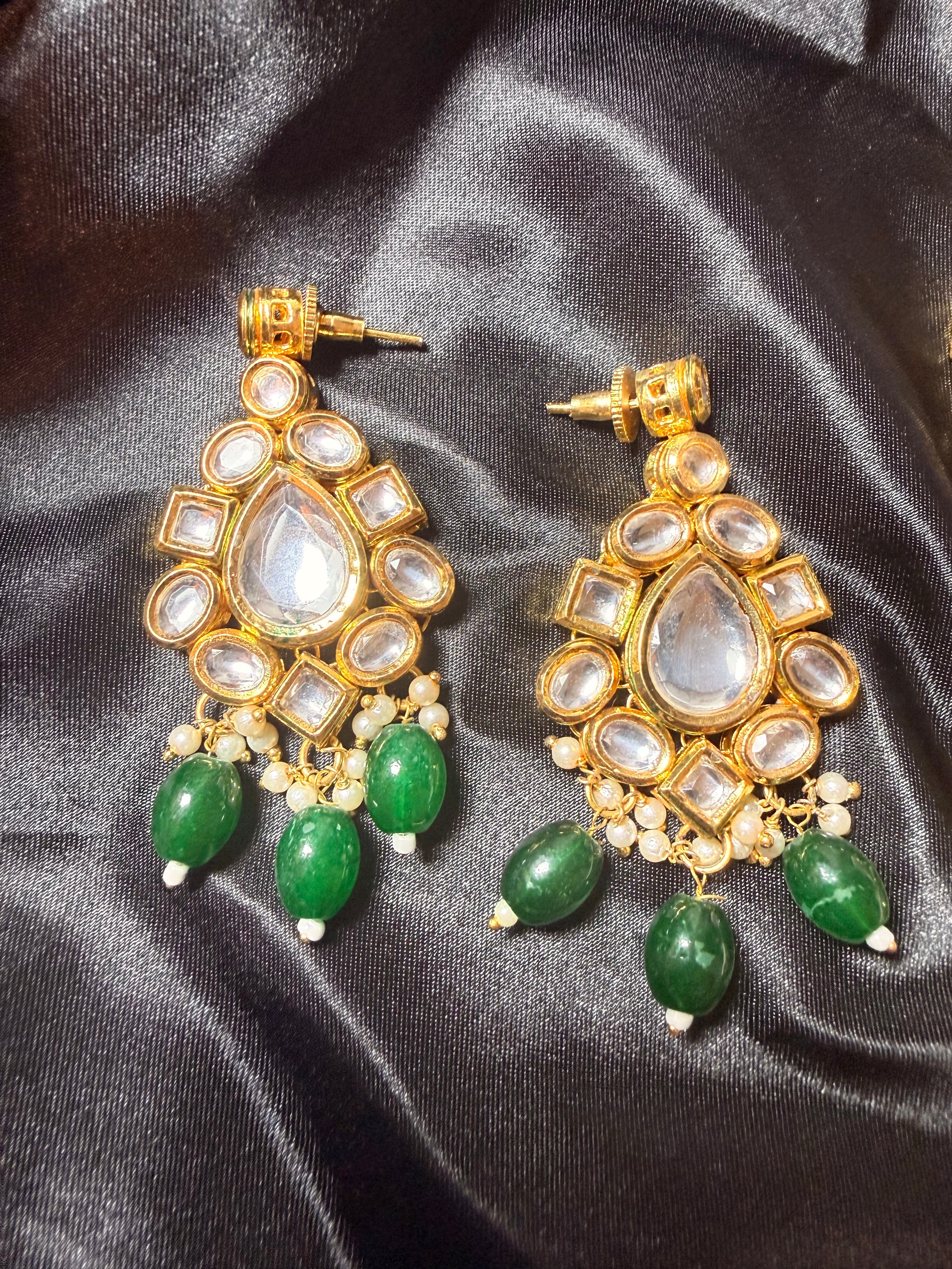 Gold and green earrings on a black satin background