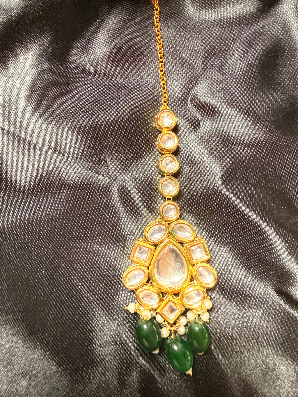 Gold necklace with green beads on a dark satin background