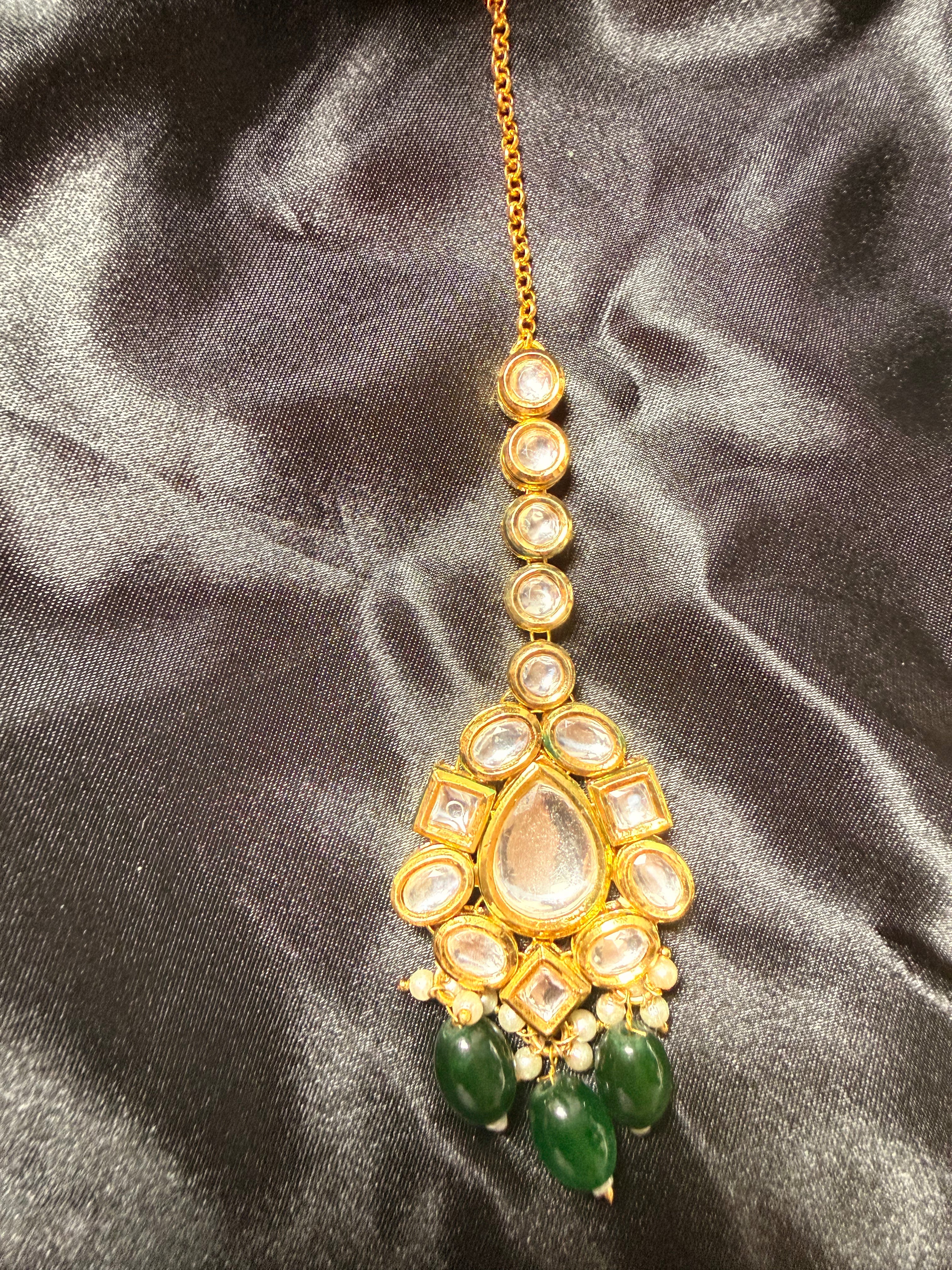 Gold necklace with green beads on a dark satin background