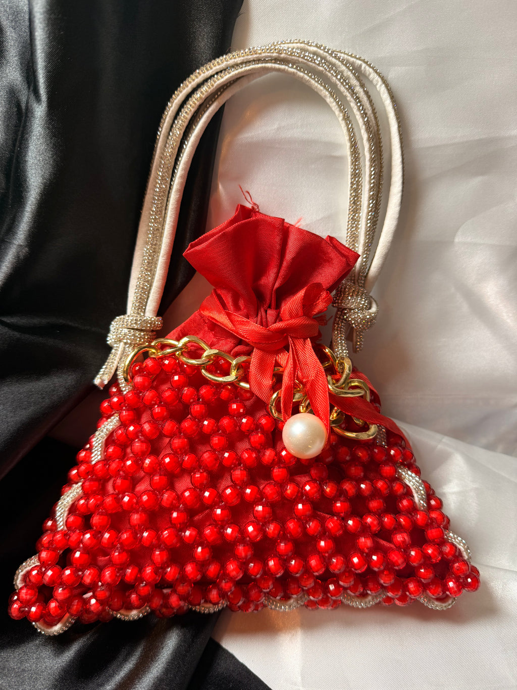 Red beaded handbag with gold accents and a red ribbon on a black and white fabric background