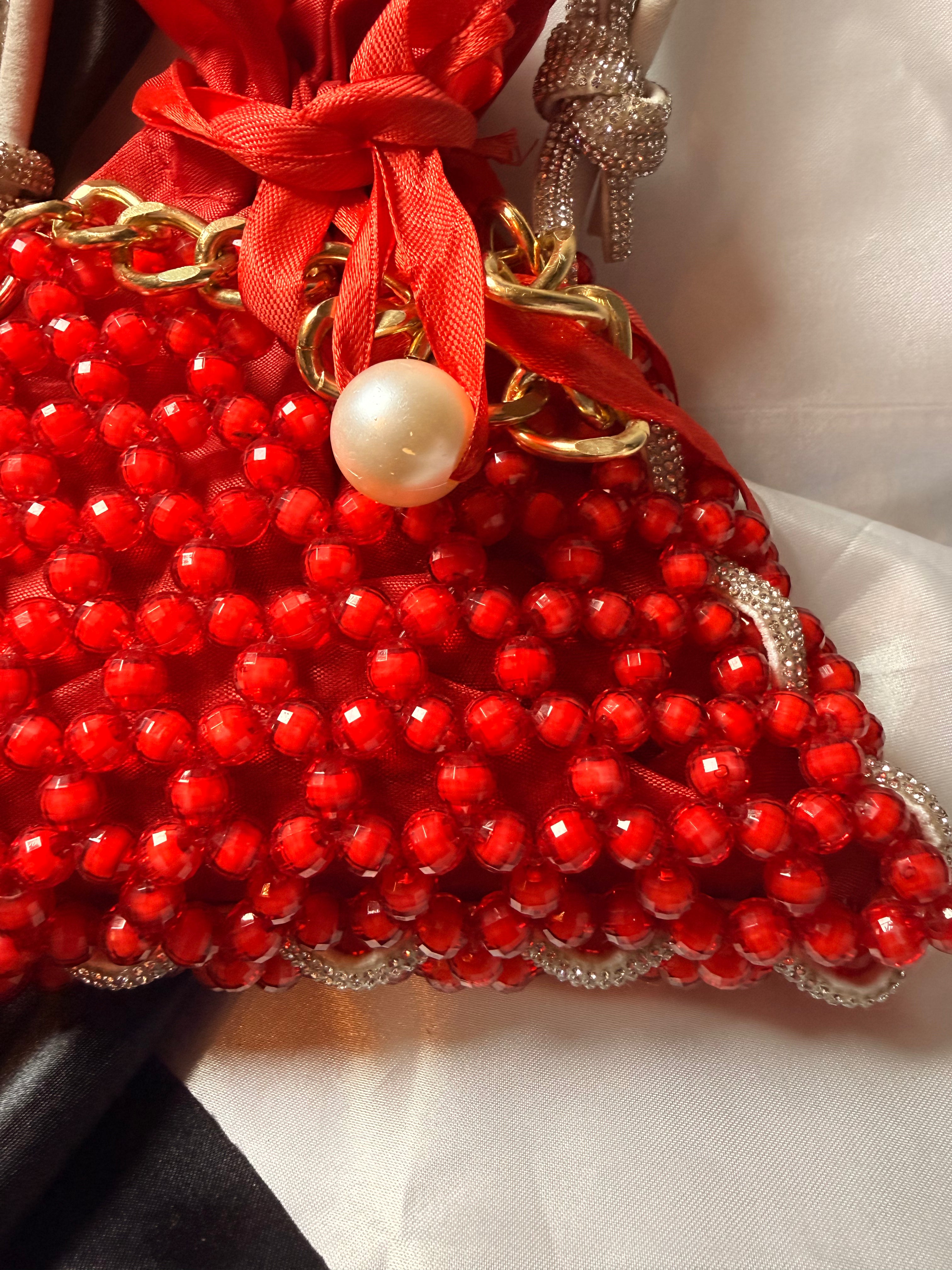 Red beaded handbag with gold chain and pearl charm on a white background