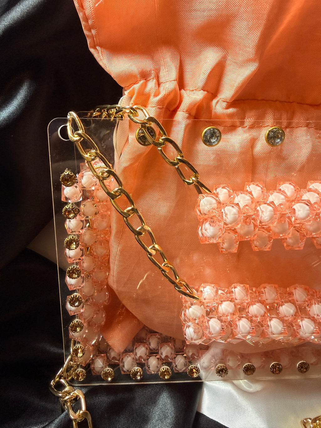 Pink handbag with gold chain strap on a black background