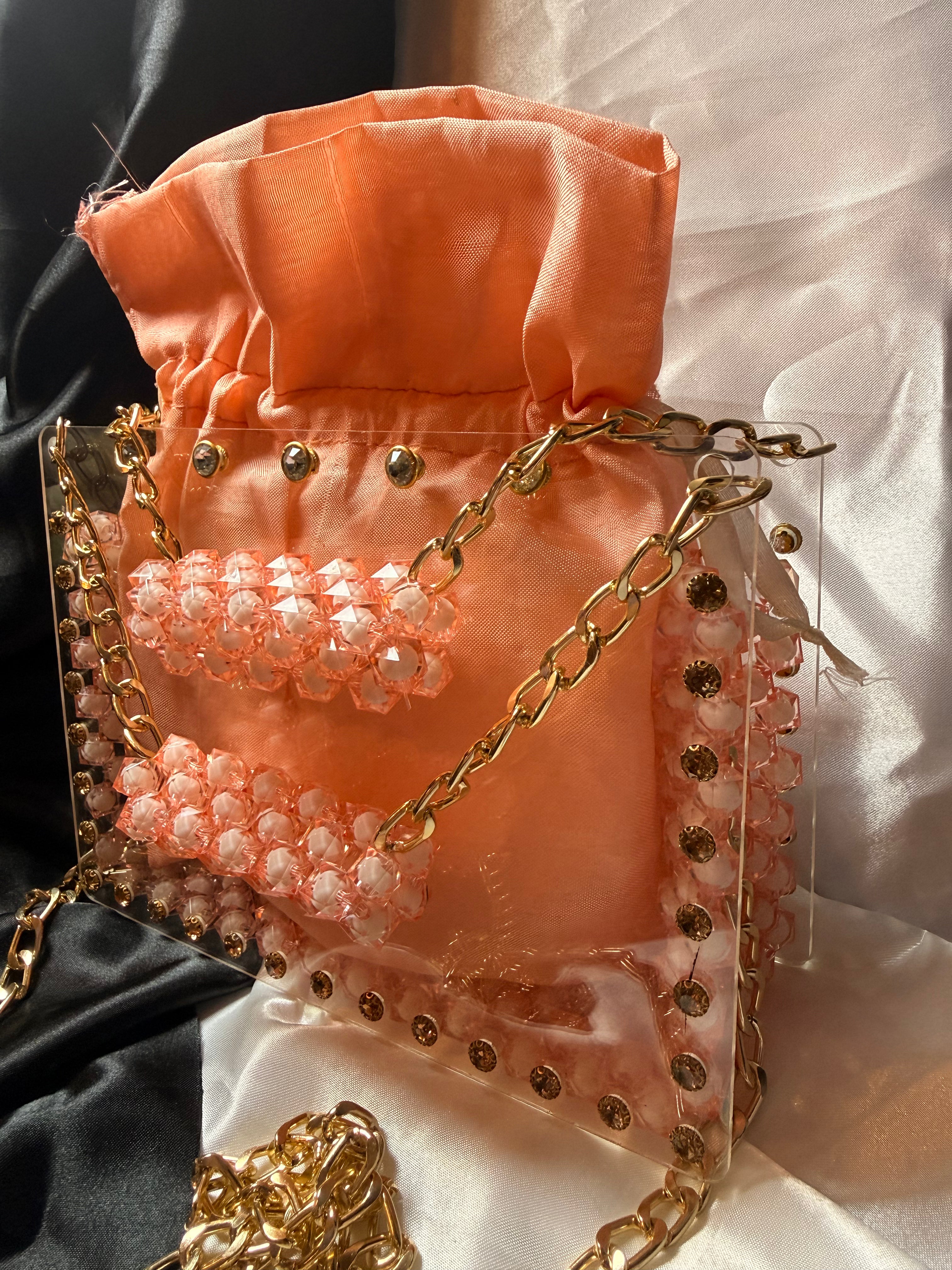 Peach-colored handbag with gold chain and embellishments on a white fabric background