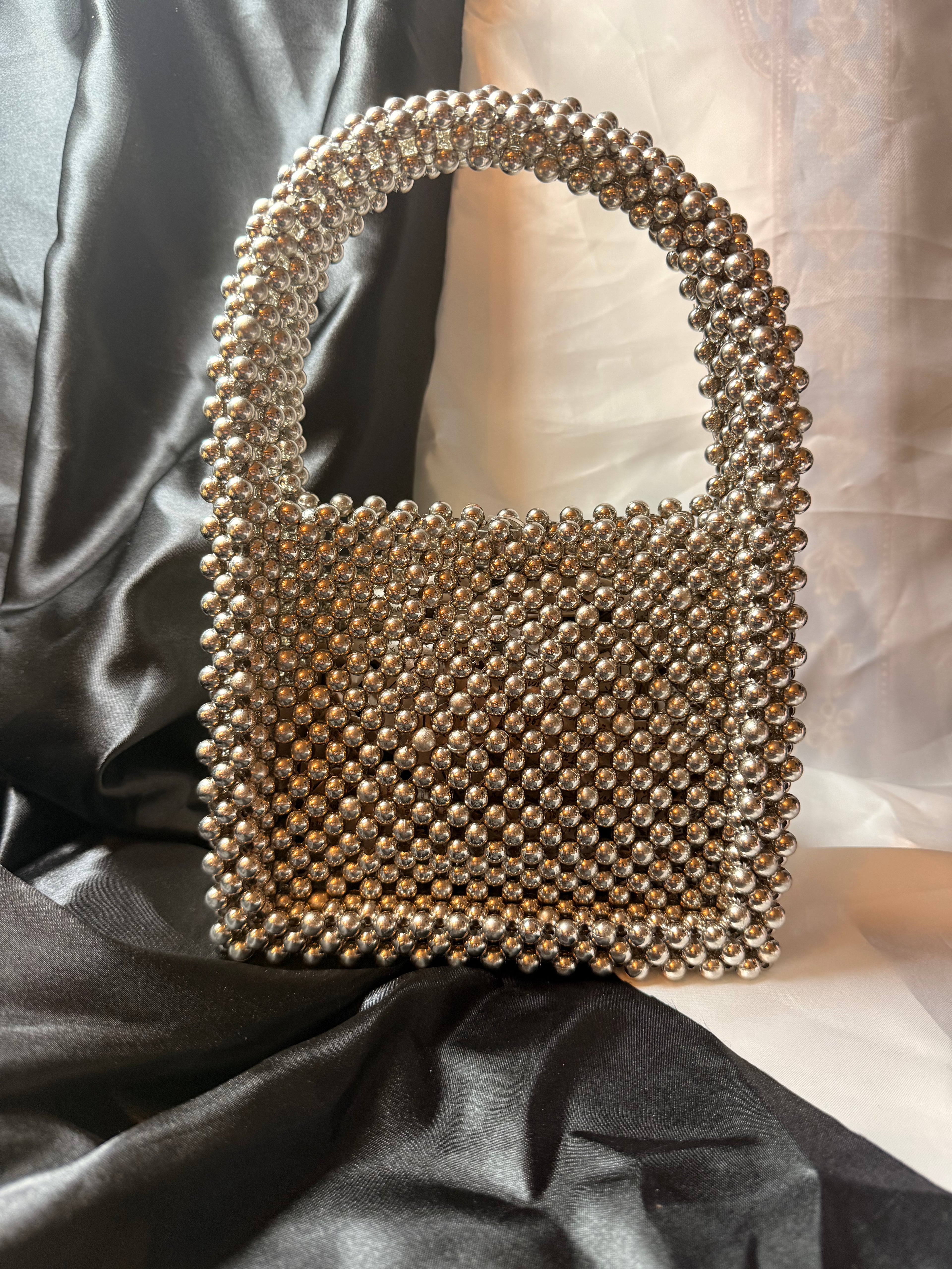 Silver beaded handbag on a black satin background
