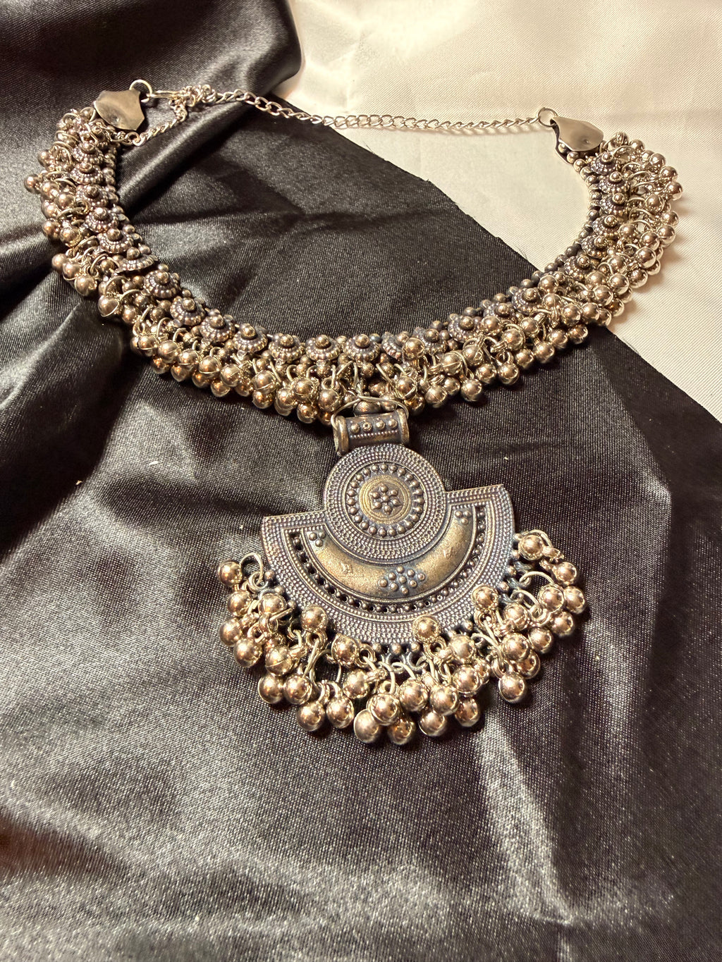 Ornate silver necklace on a dark fabric background