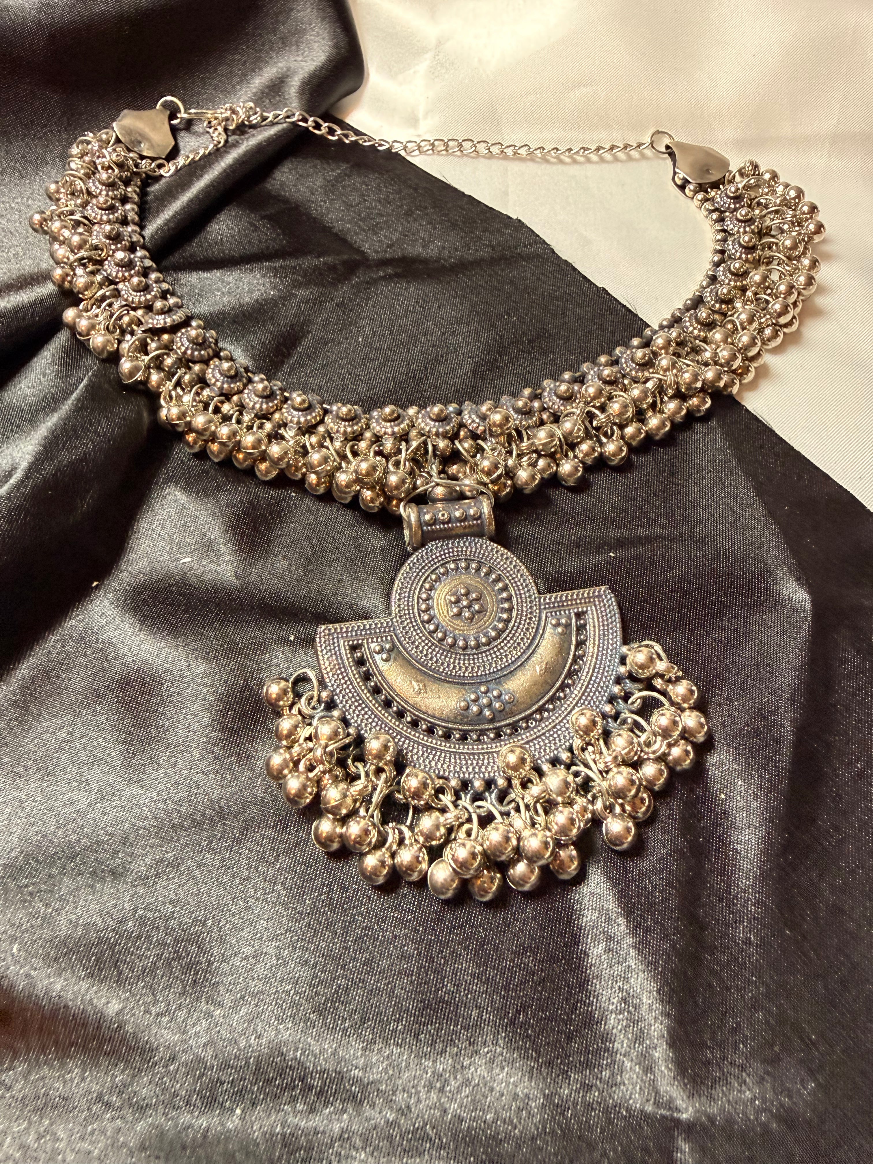 Ornate silver necklace on a dark fabric background
