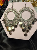 Pair of ornate earrings with coin details on a pink card against a black satin background.