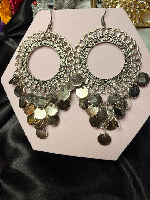 Pair of ornate earrings with coin details on a pink card against a black satin background.