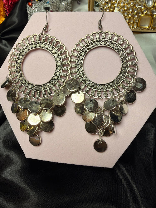 Pair of ornate earrings with coin details on a pink card against a black background