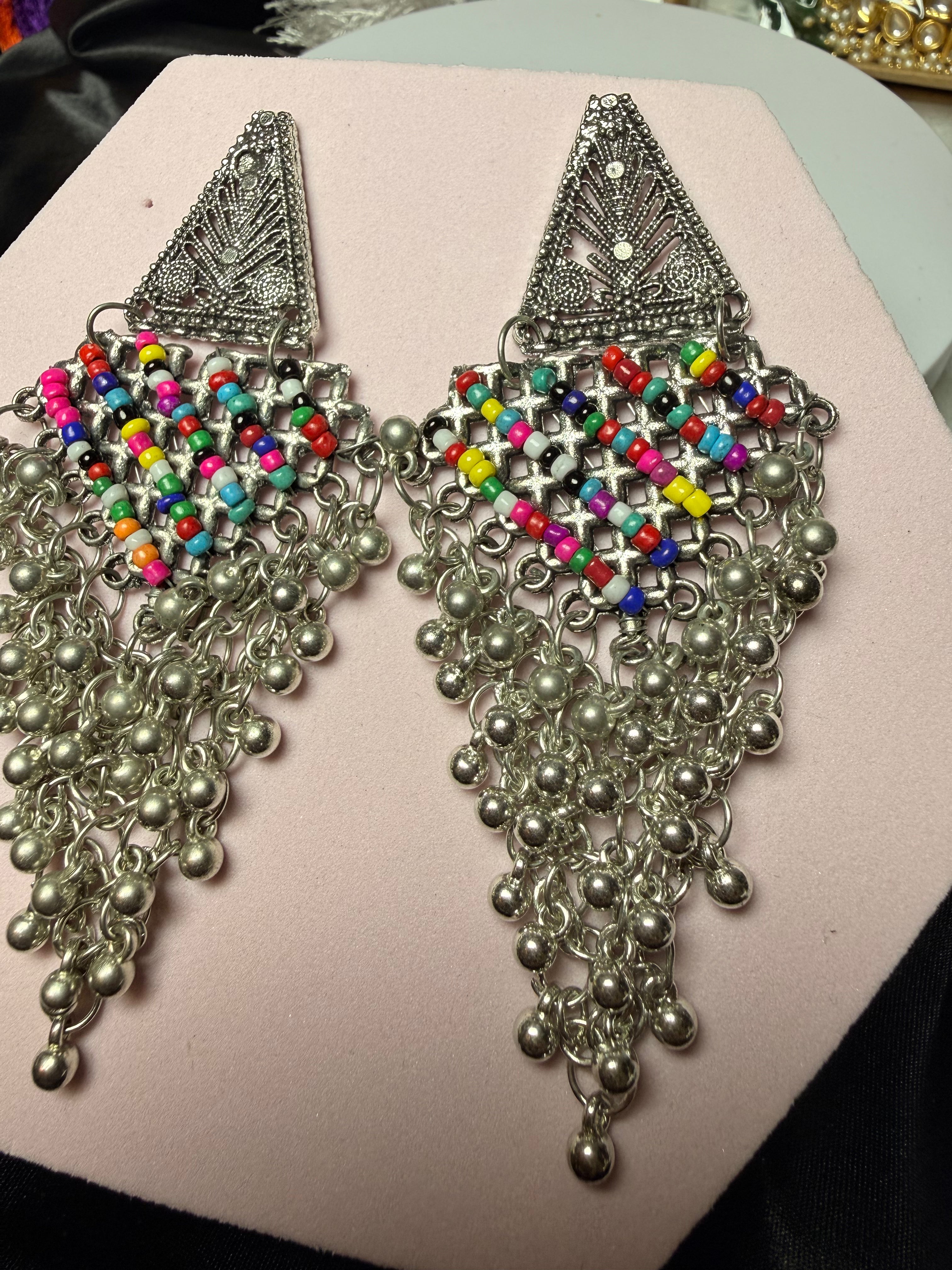 Pair of ornate silver earrings with colorful beads on a pink surface