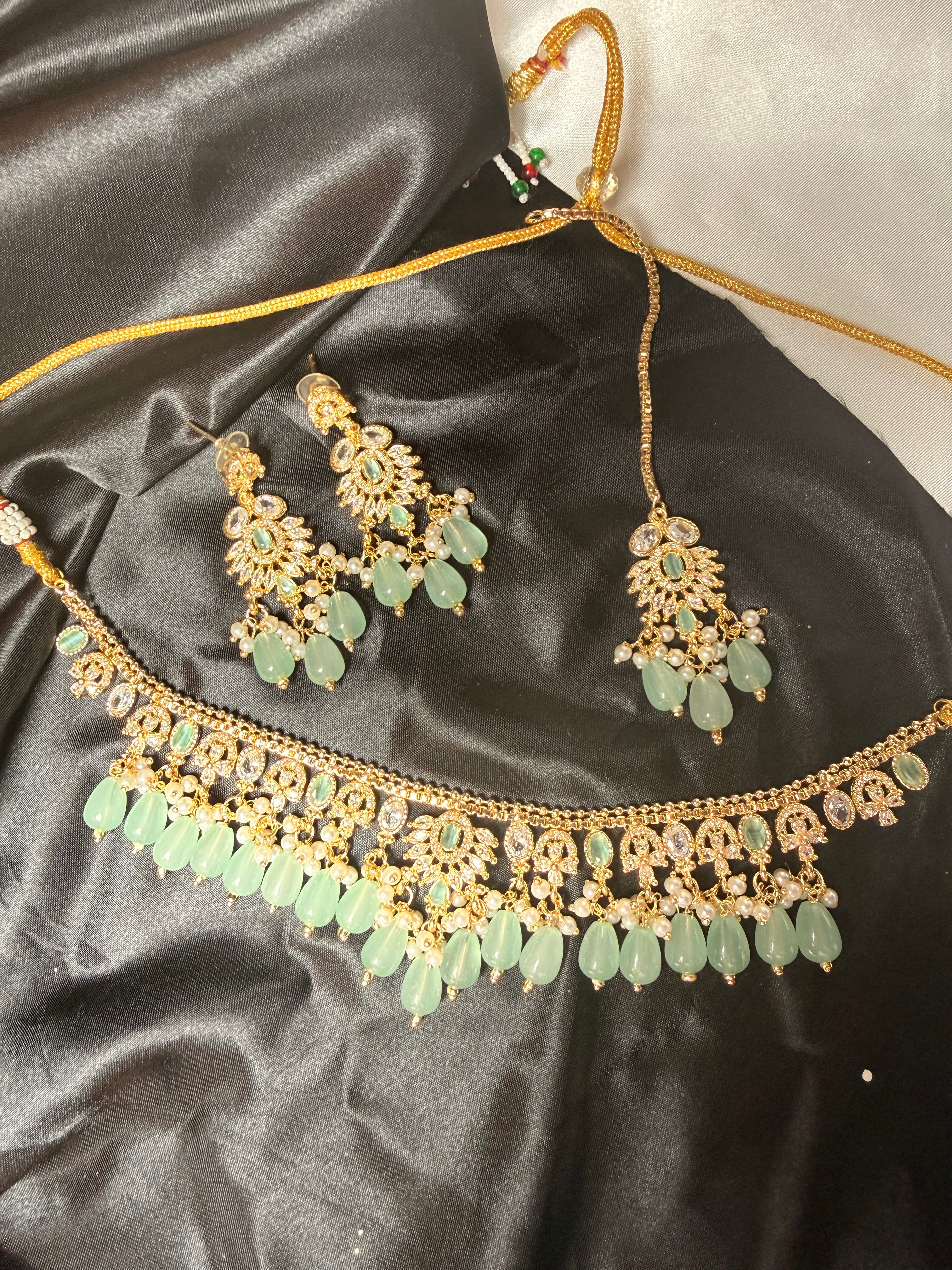 Gold and green jewelry set on a black satin surface