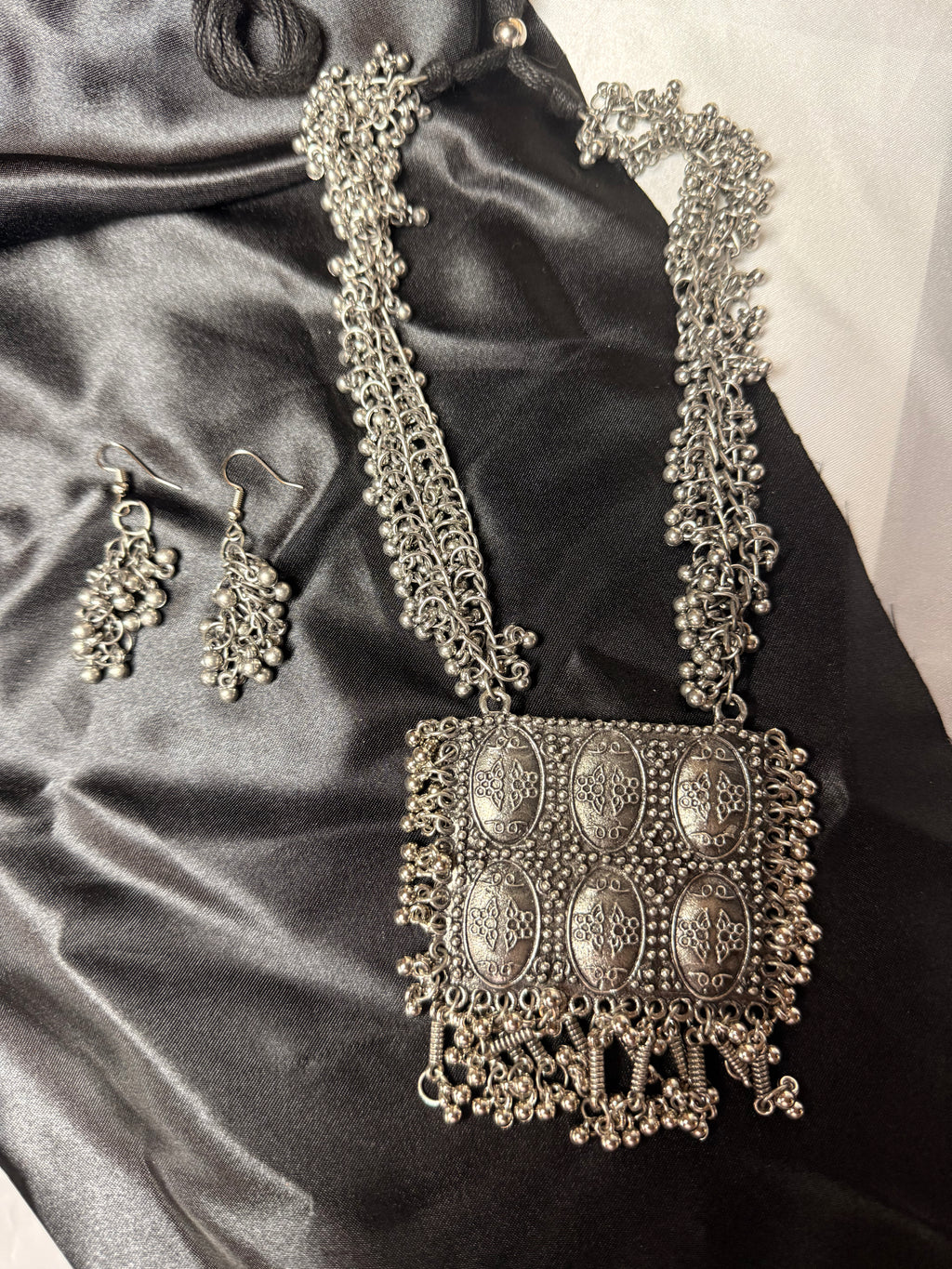 Decorative silver handbag and earrings on a satin surface