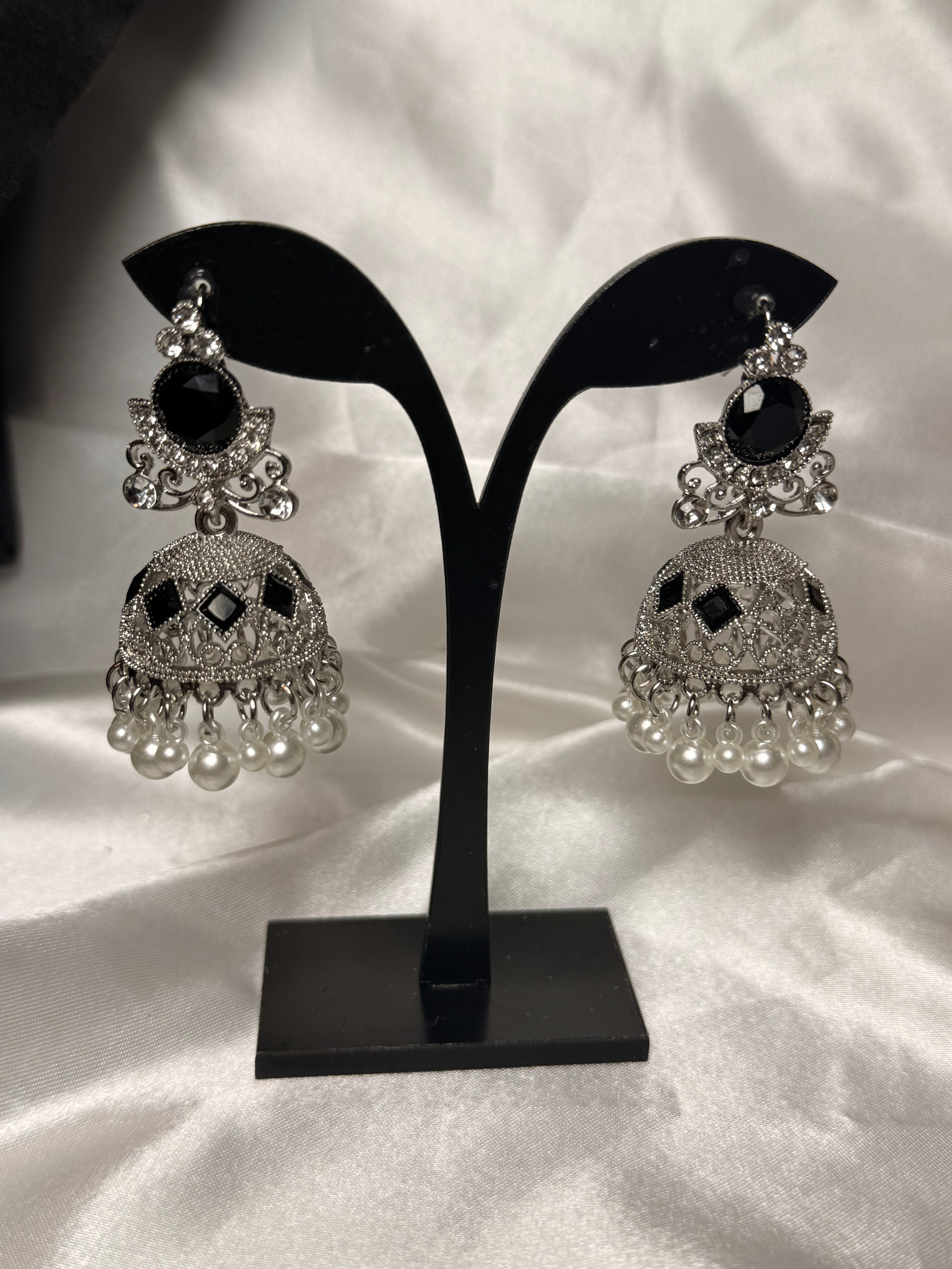 Pair of silver and black earrings on a black stand against a white background