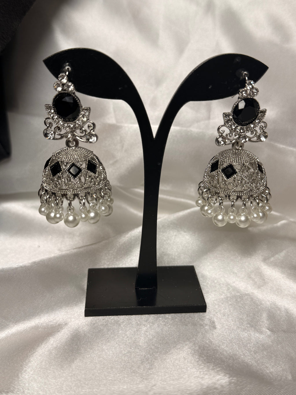 Pair of silver earrings with black and pearl accents on a black stand against a white background
