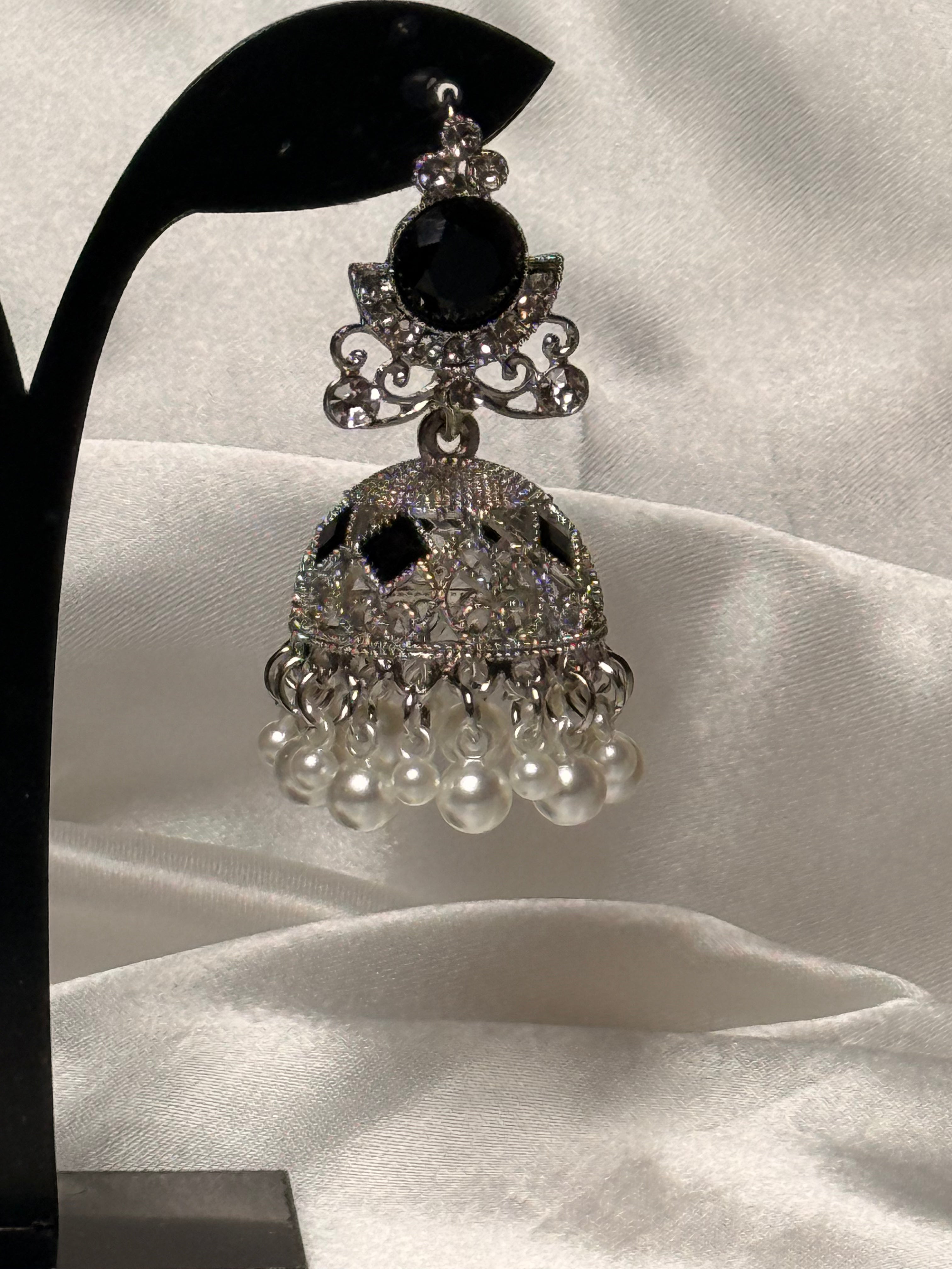 Ornate silver earring with black gemstone and pearl-like beads on a white fabric background