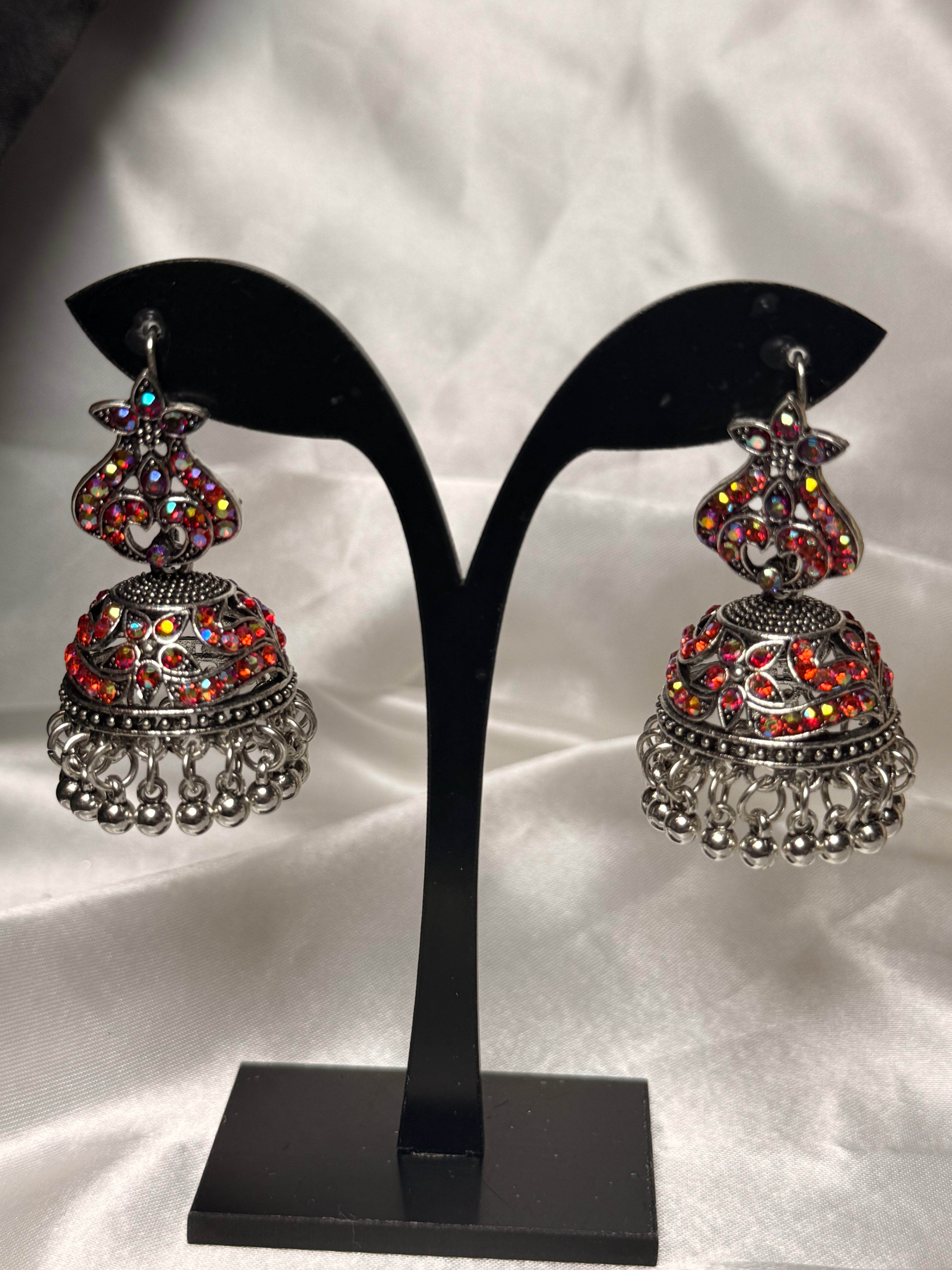 Pair of silver and red beaded earrings on a black stand against a white background