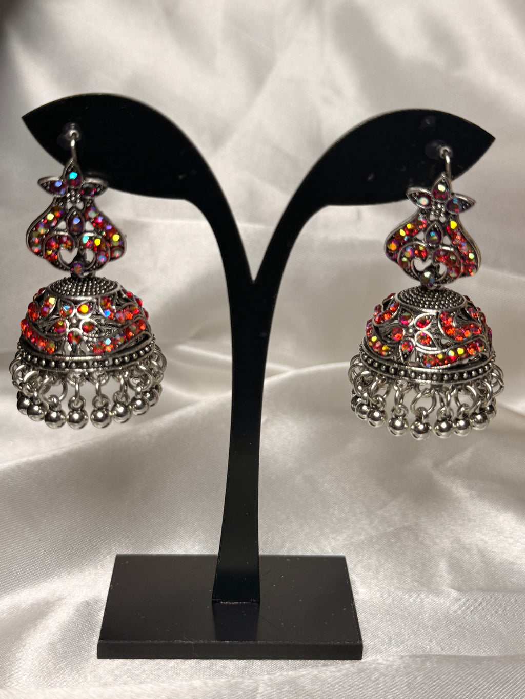 Pair of ornate earrings on a black earring stand against a white background