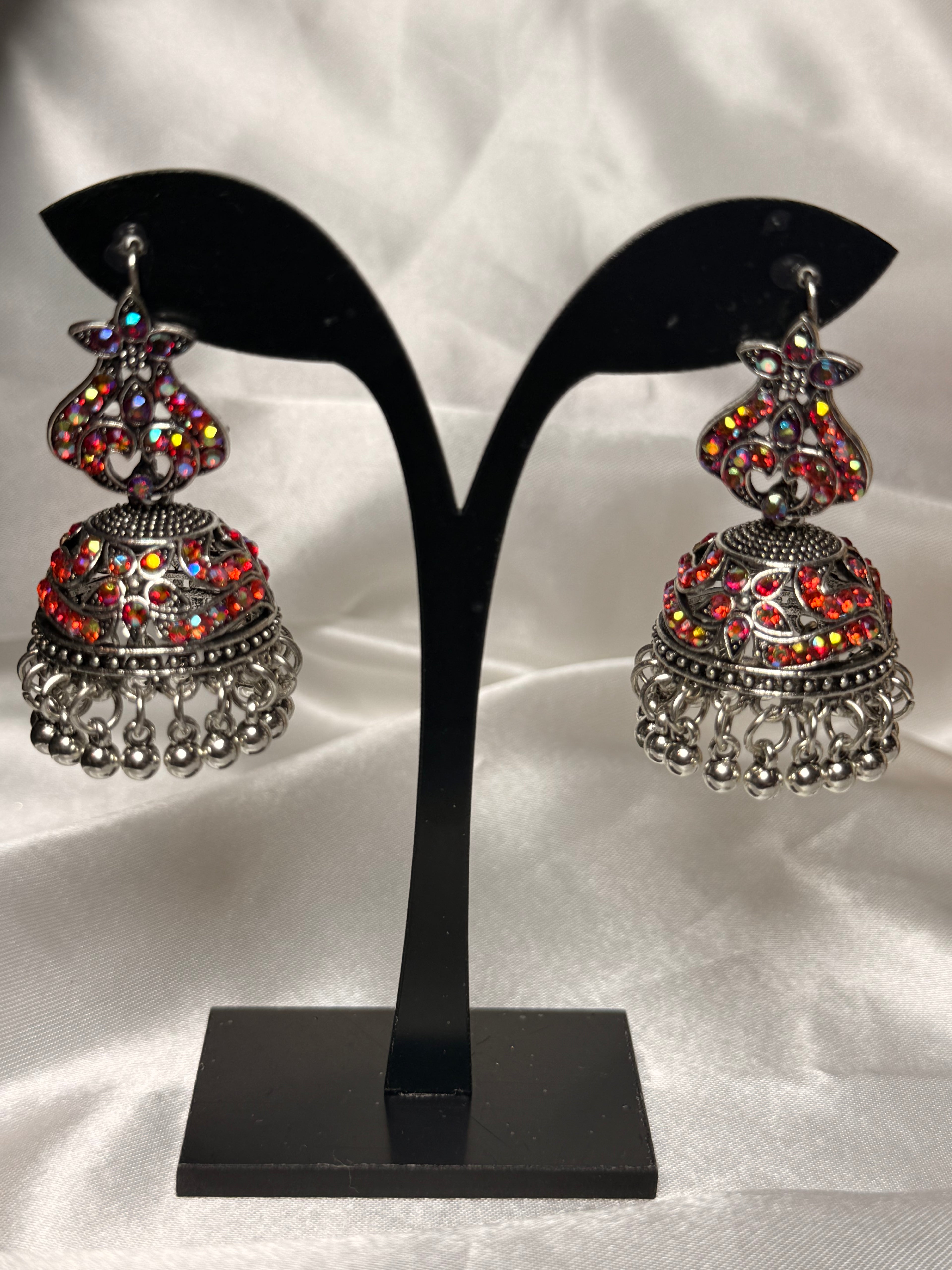 Pair of ornate earrings on a black earring stand against a white background