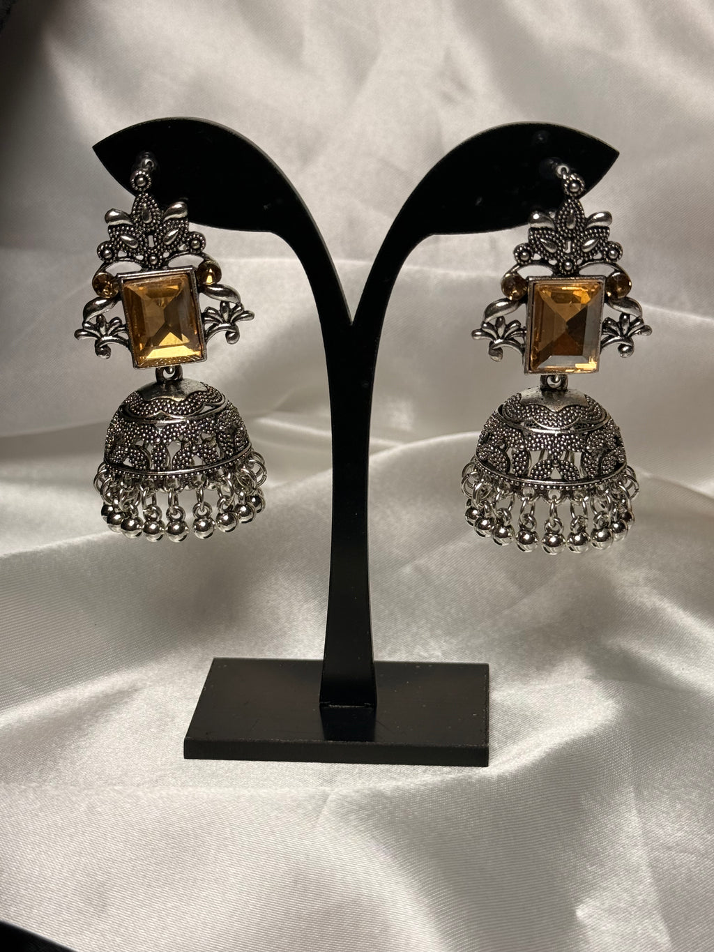 Pair of ornate earrings on a black stand against a white background