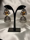 Pair of ornate earrings on a black stand against a white background
