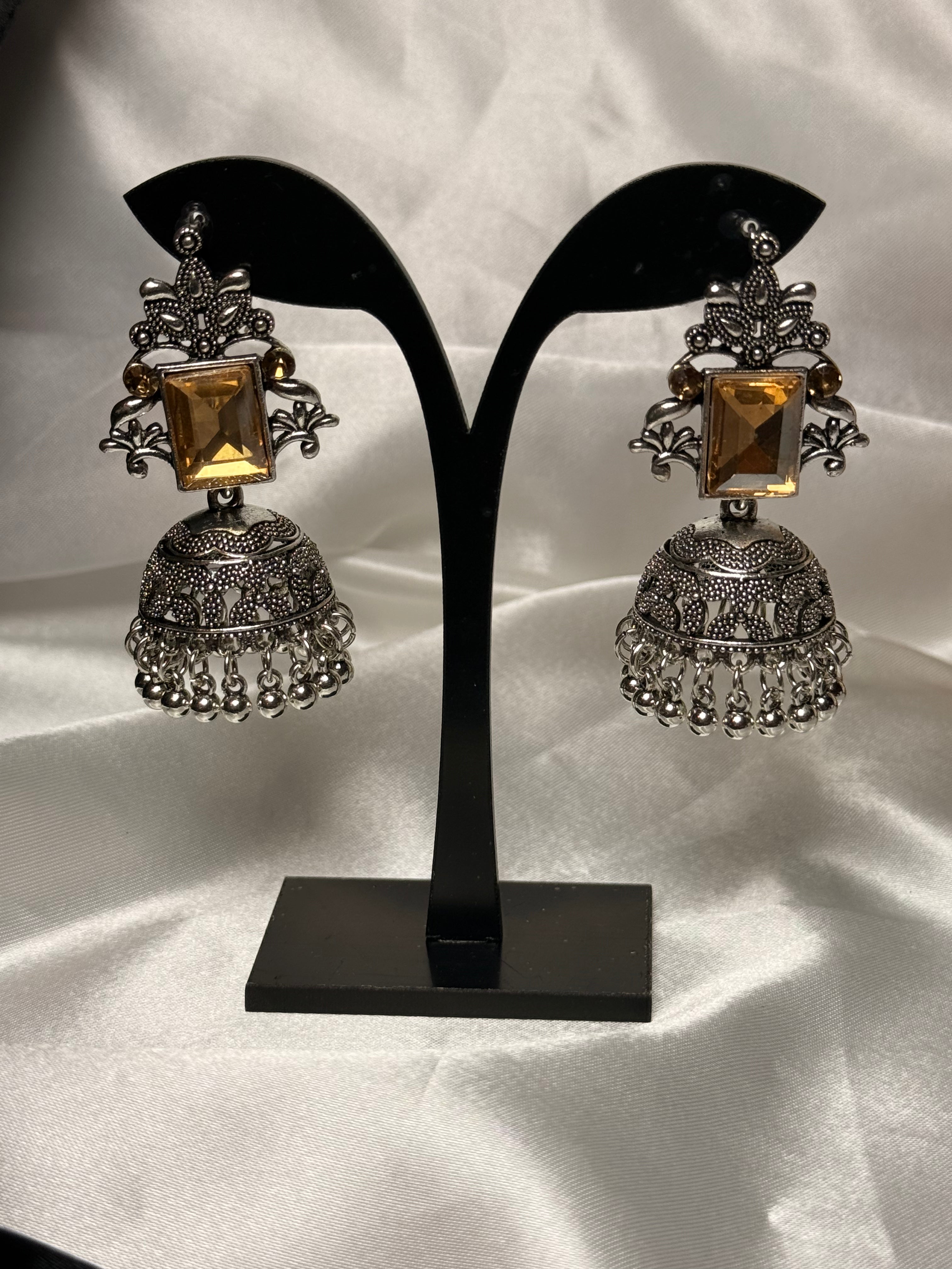 Pair of ornate earrings on a black stand against a white background