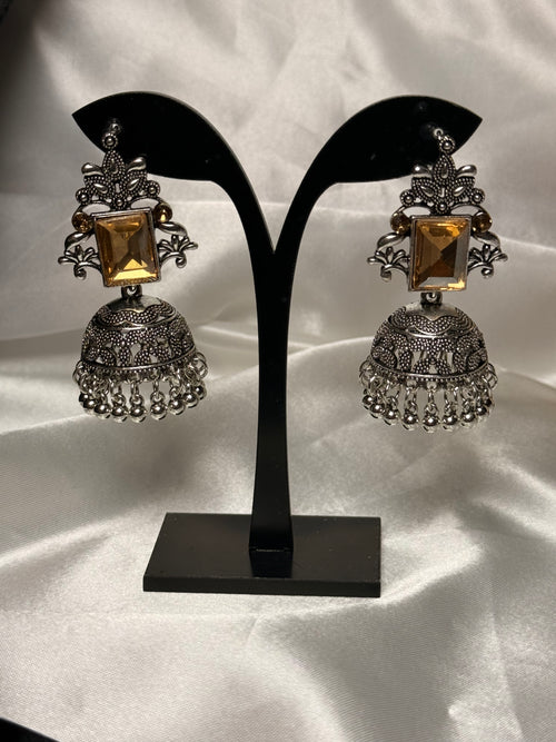 Pair of ornate earrings on a black stand against a white background