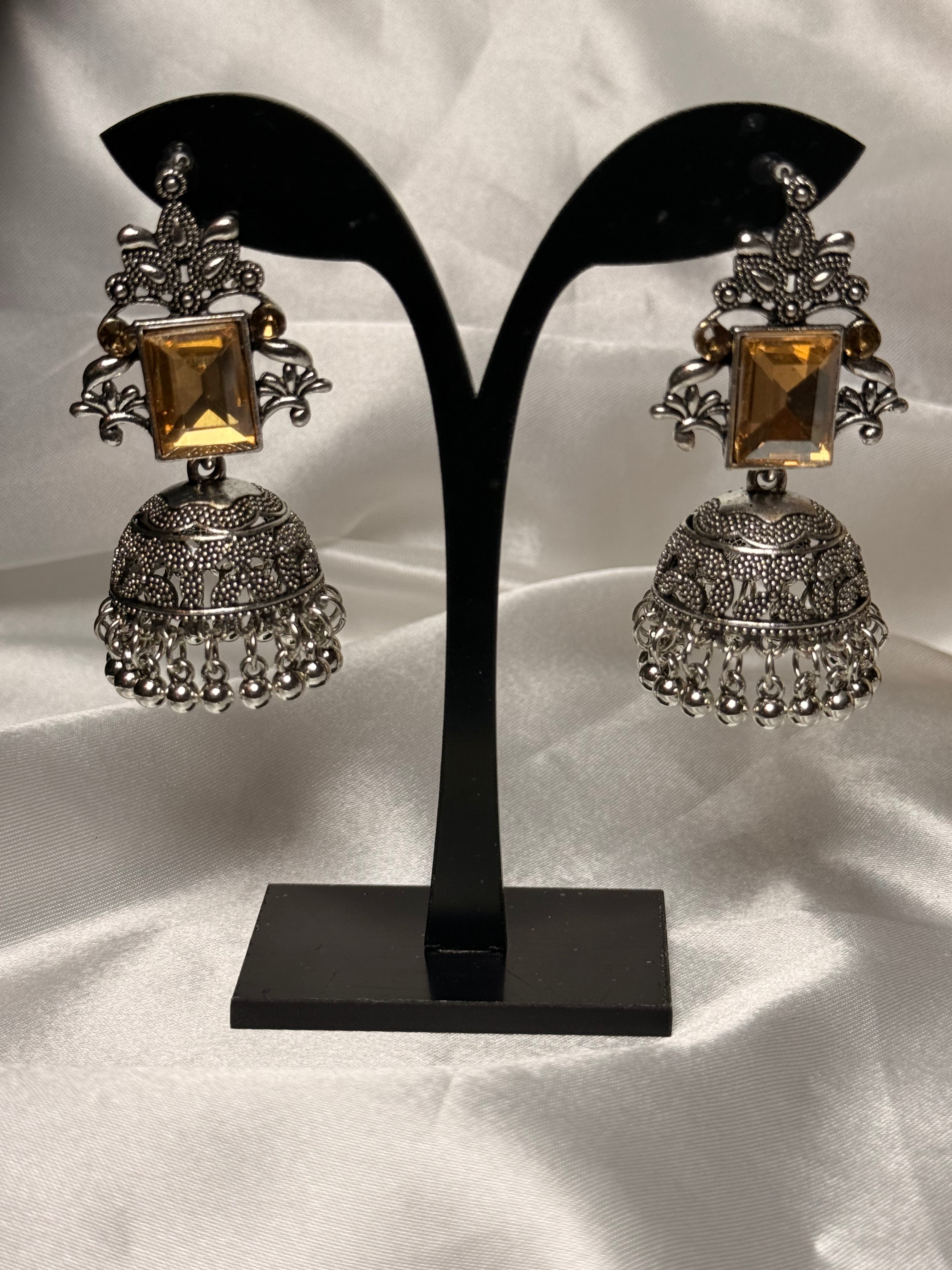 Pair of silver and gold earrings on a black stand against a white background