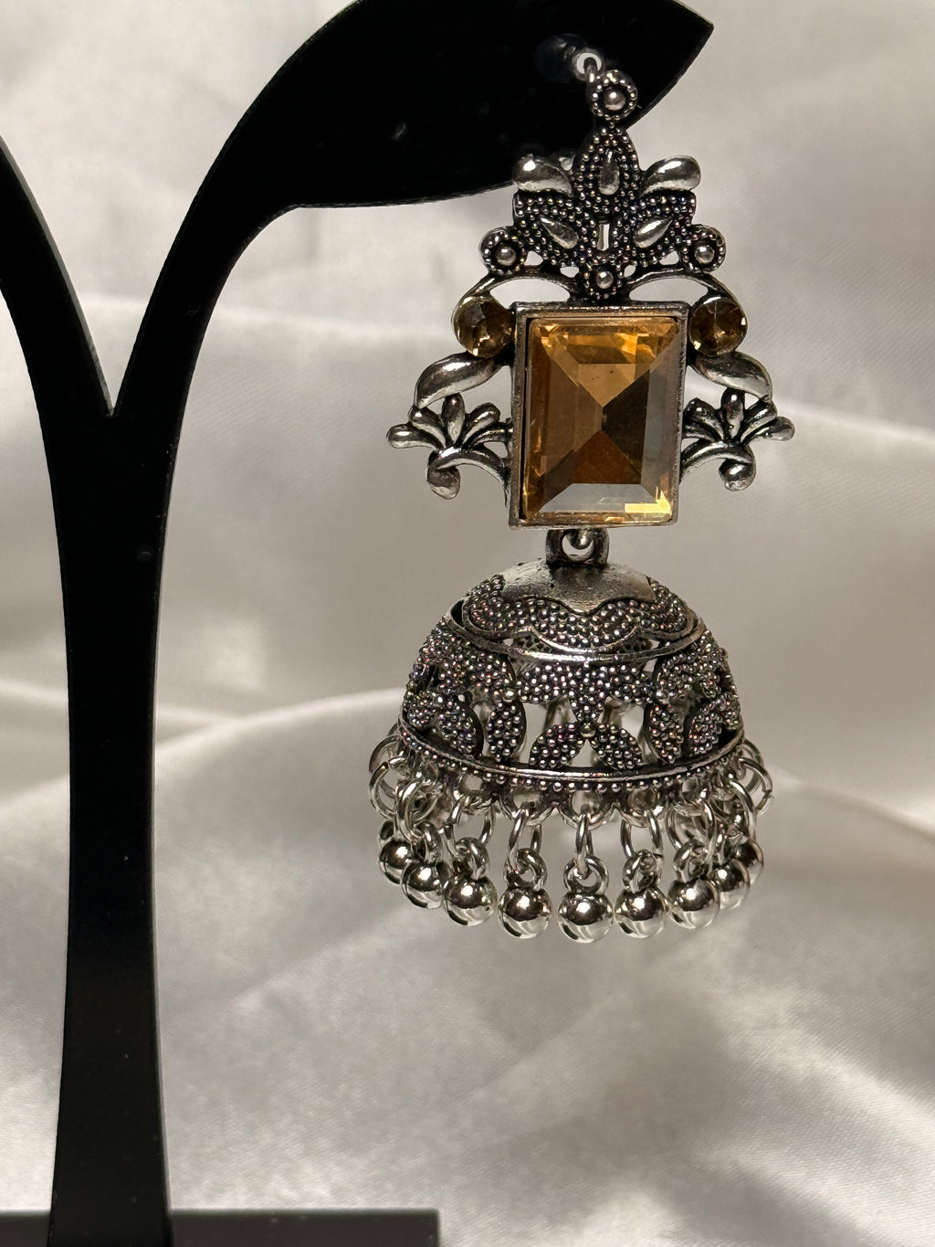 Silver and amber gemstone earring on a black stand against a white background
