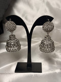 Pair of silver jhumka earrings on a black stand against a white fabric background