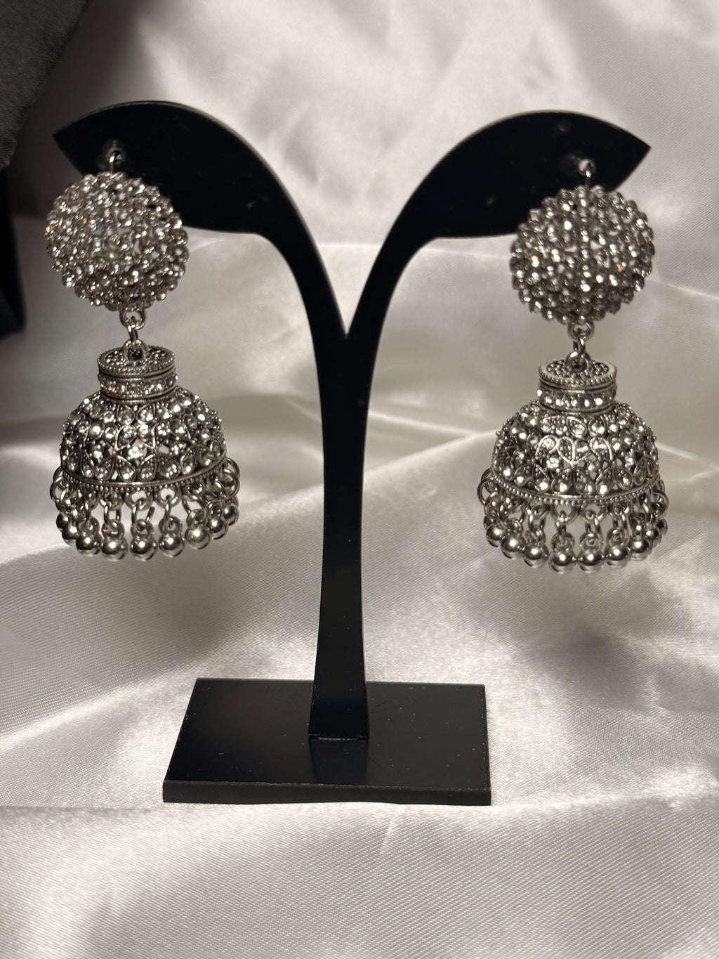 Pair of silver jhumka earrings on a black earring stand against a white satin background