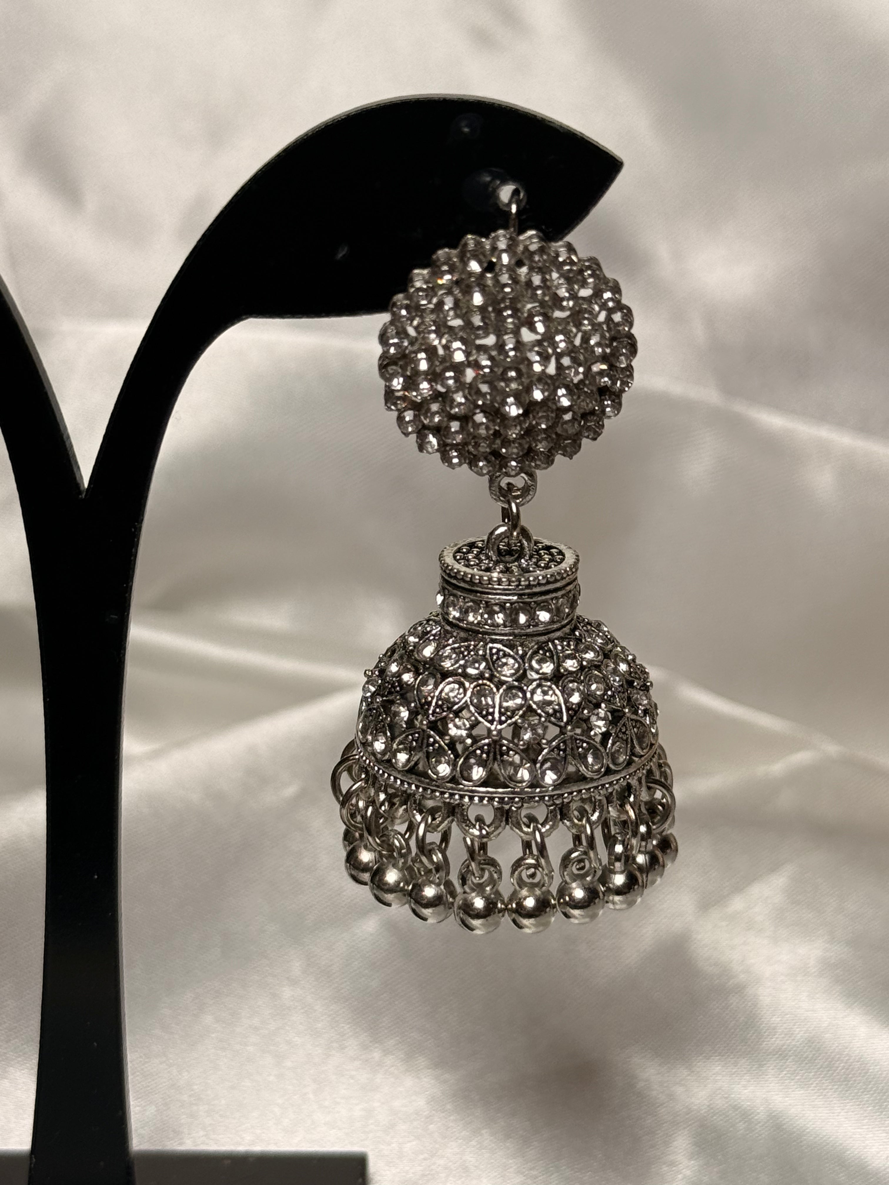 Silver jhumka earring on a white fabric background