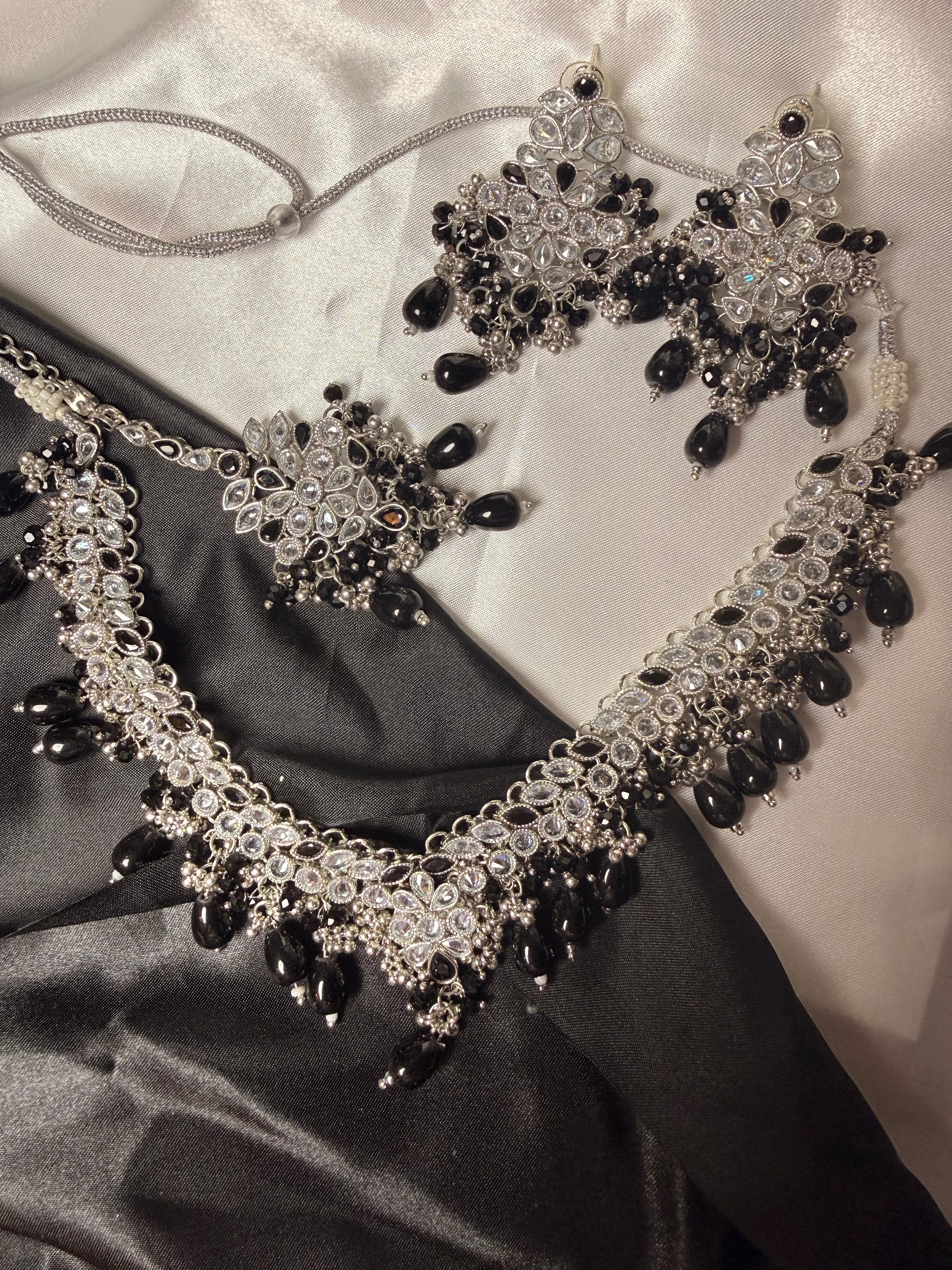 Ornate necklace with black and clear stones on a satin surface