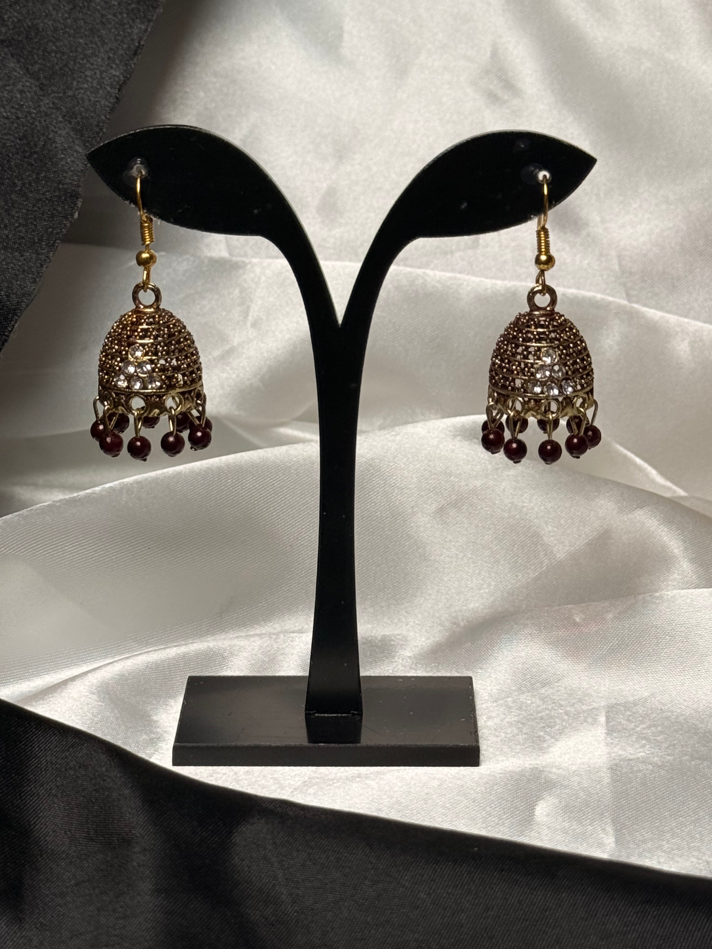 Pair of gold and brown earrings on a black earring stand against a white fabric background