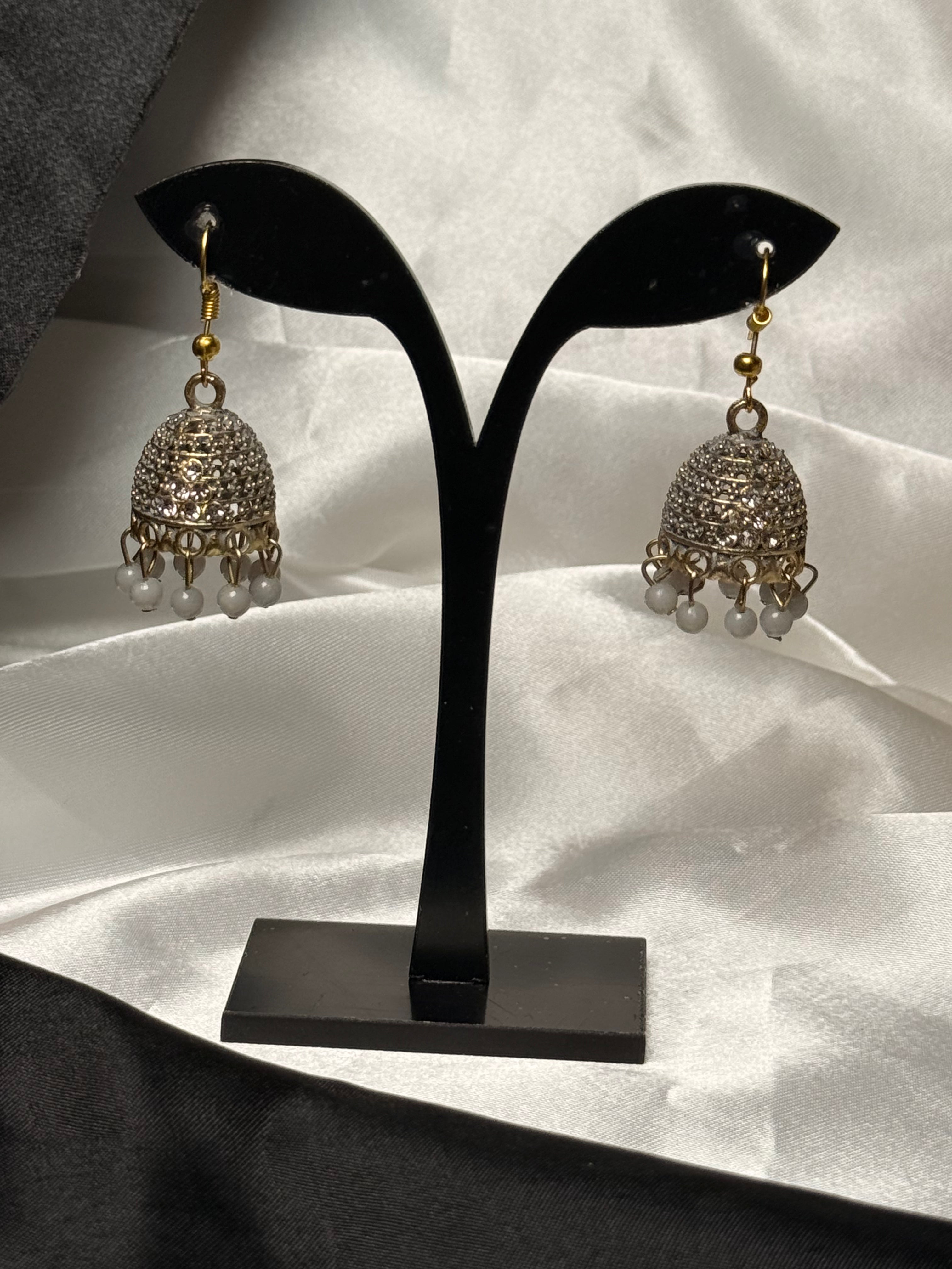 Pair of silver jhumka earrings on a black earring stand against a white fabric background
