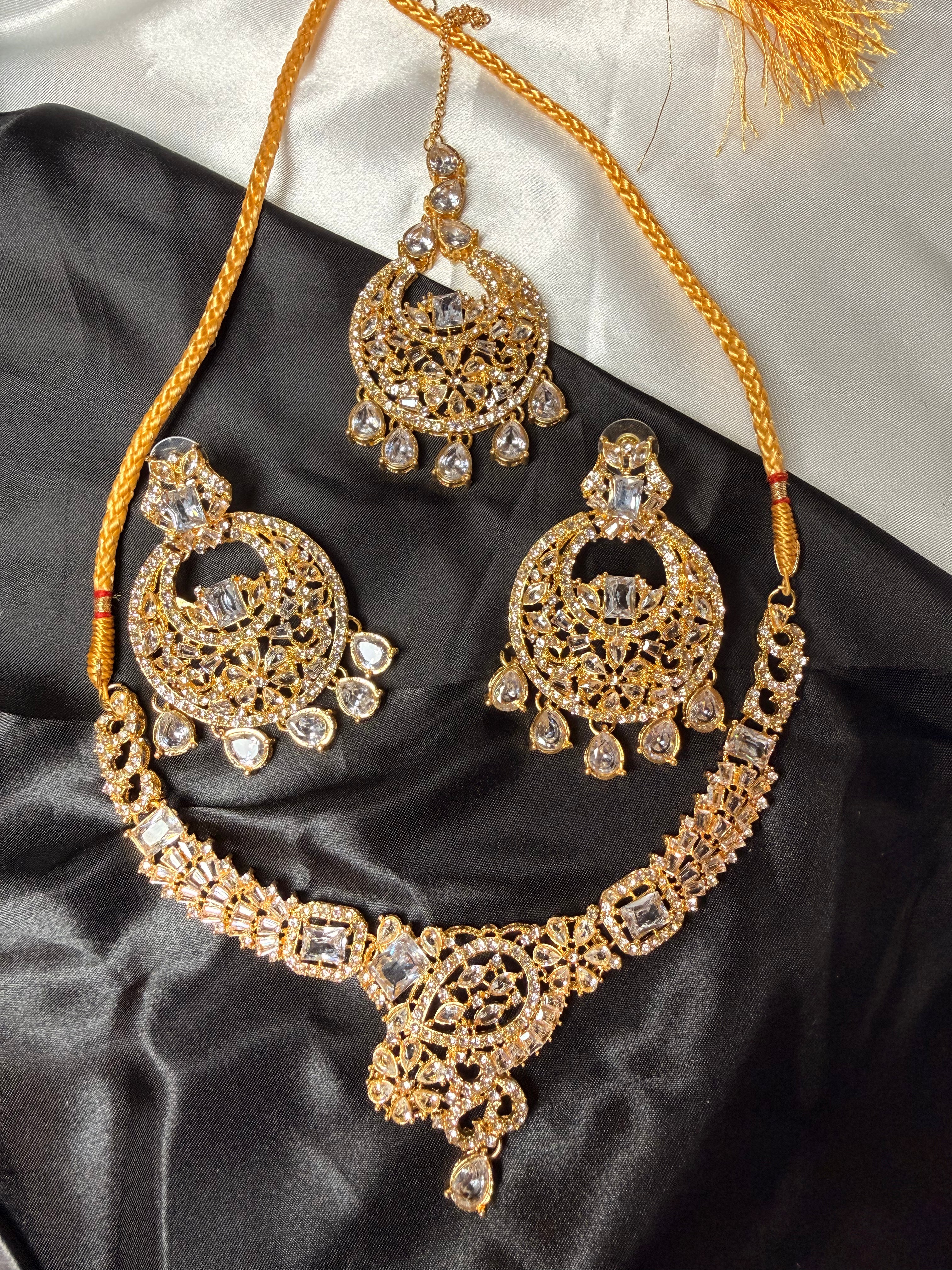 Ornate gold necklace and earrings on a black satin surface