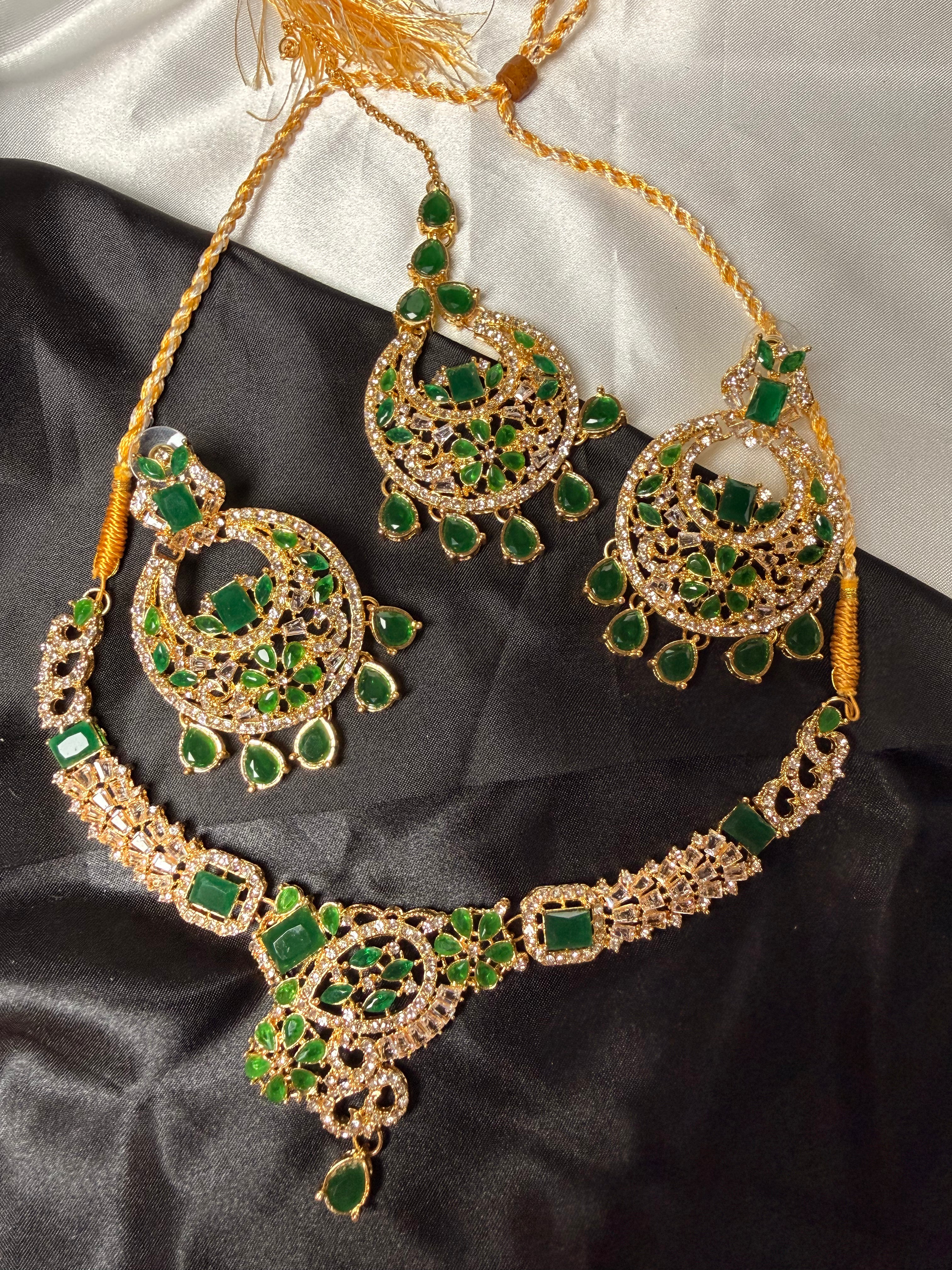 Ornate necklace with green gemstones on a black satin surface