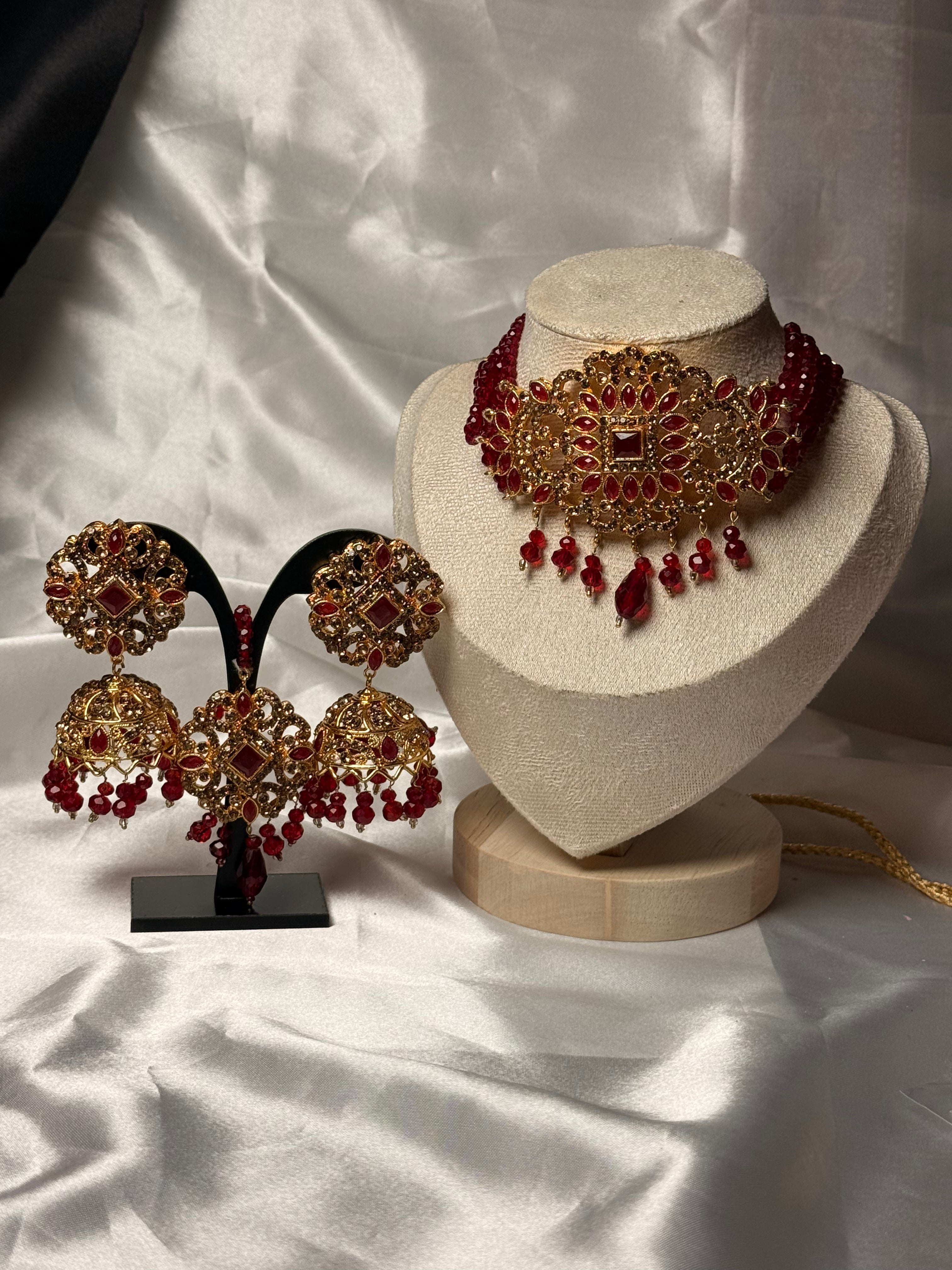 Jewelry set with red and gold necklace and earrings on a mannequin and stand against a white fabric background.