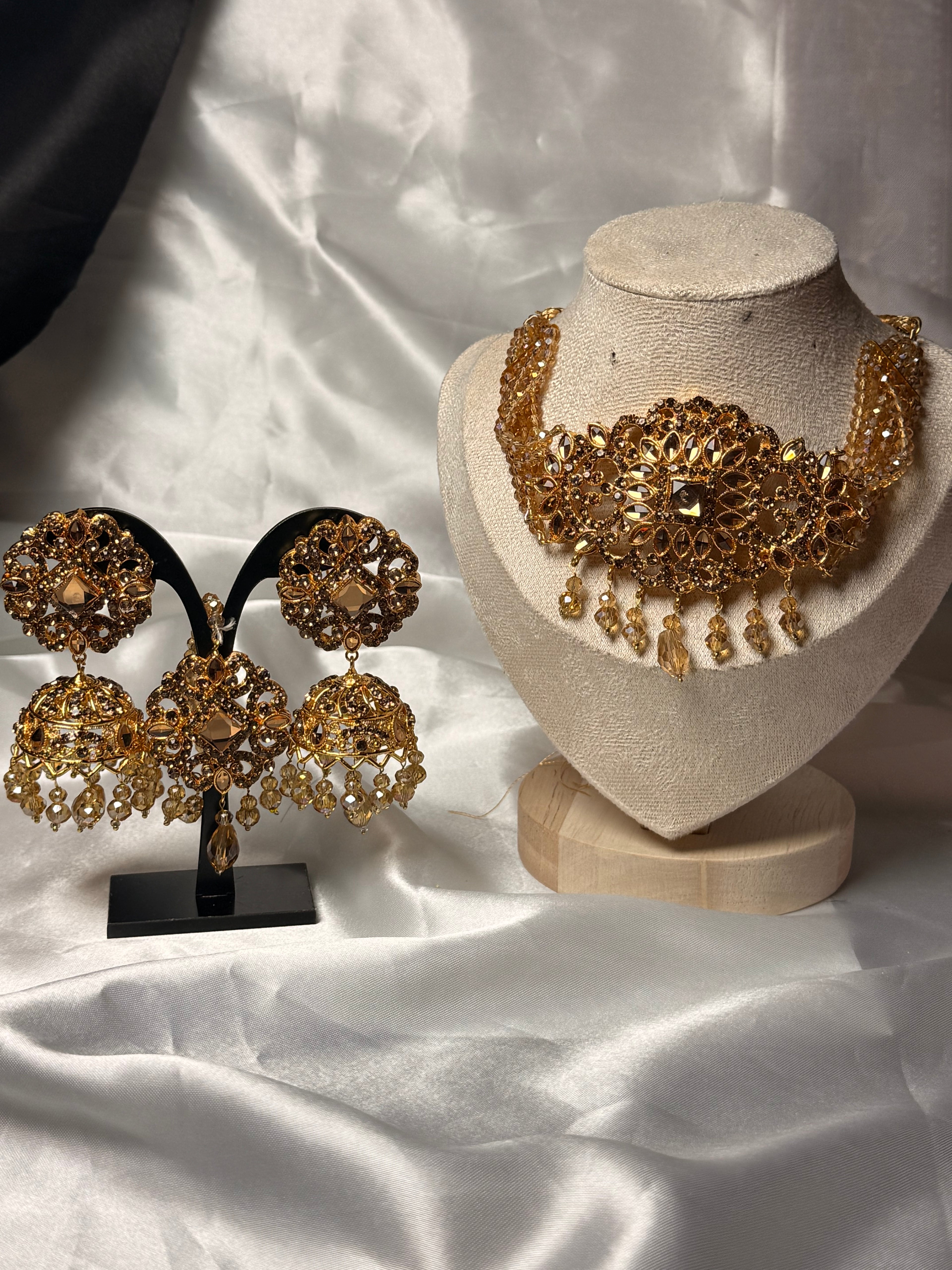 Gold jewelry set including earrings and a necklace on a white fabric background